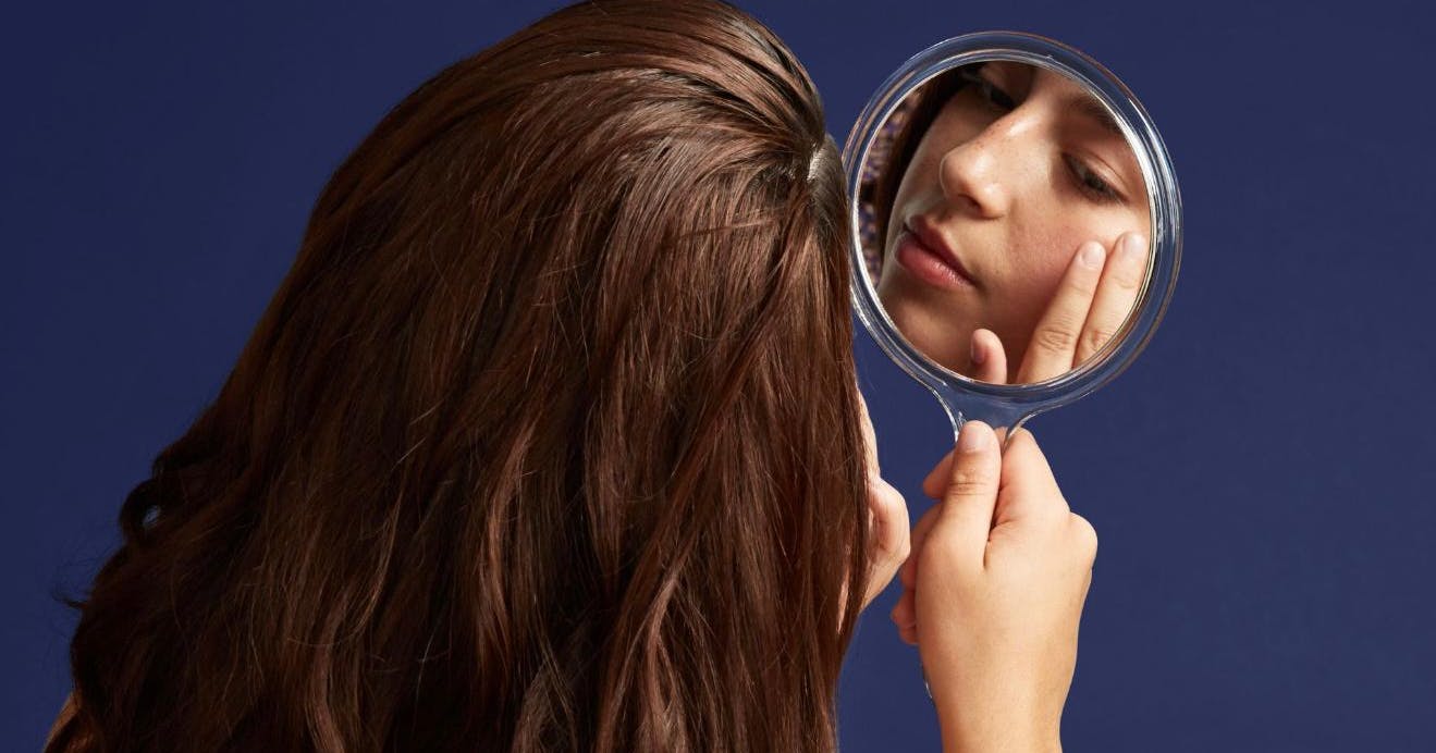A female patient looking at her red carpet facial results in the mirror