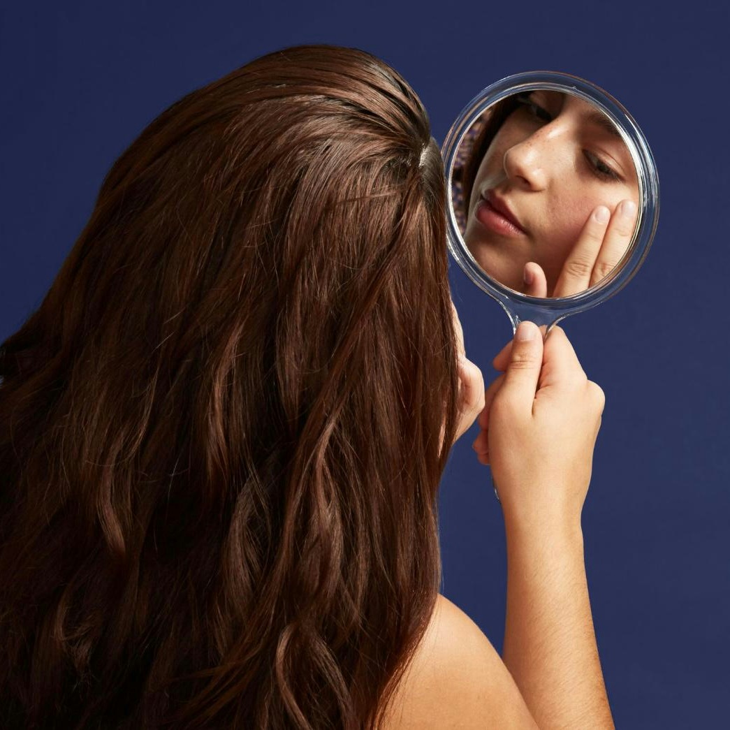 A female patient looking at her red carpet facial results in the mirror