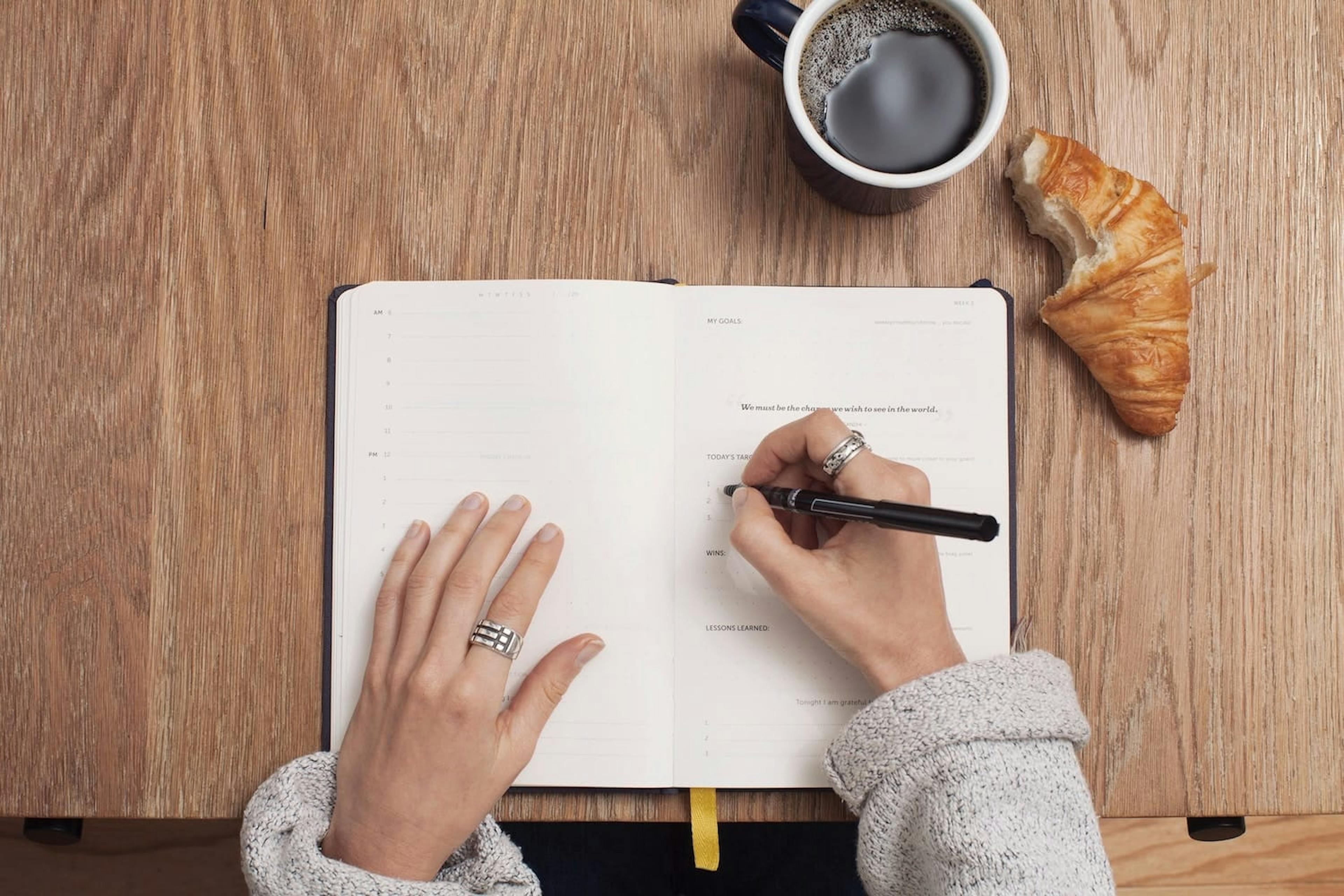 Mujer tomando apuntes con cafe y croissant