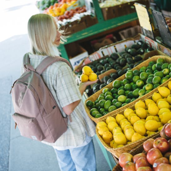 A woman buying lemons wearing a backpack