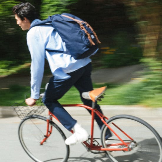 A man riding a red bike wearing a blue Herschel backpack