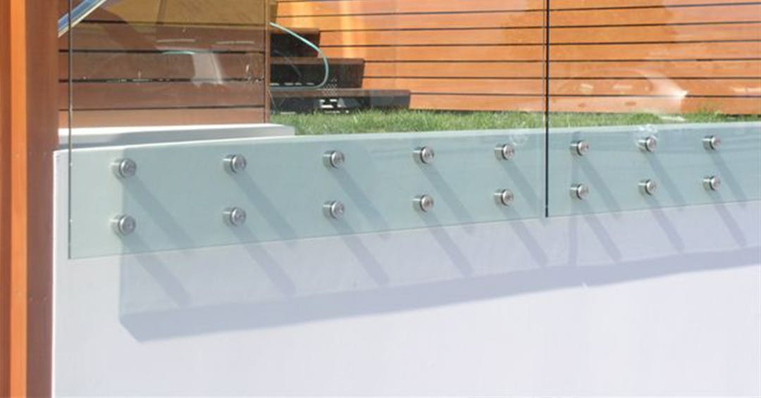 Frameless glass balustrade fixed with stainless steel handrail fittings, mounted on a low wall to provide secure and clean boundaries in outdoor areas.