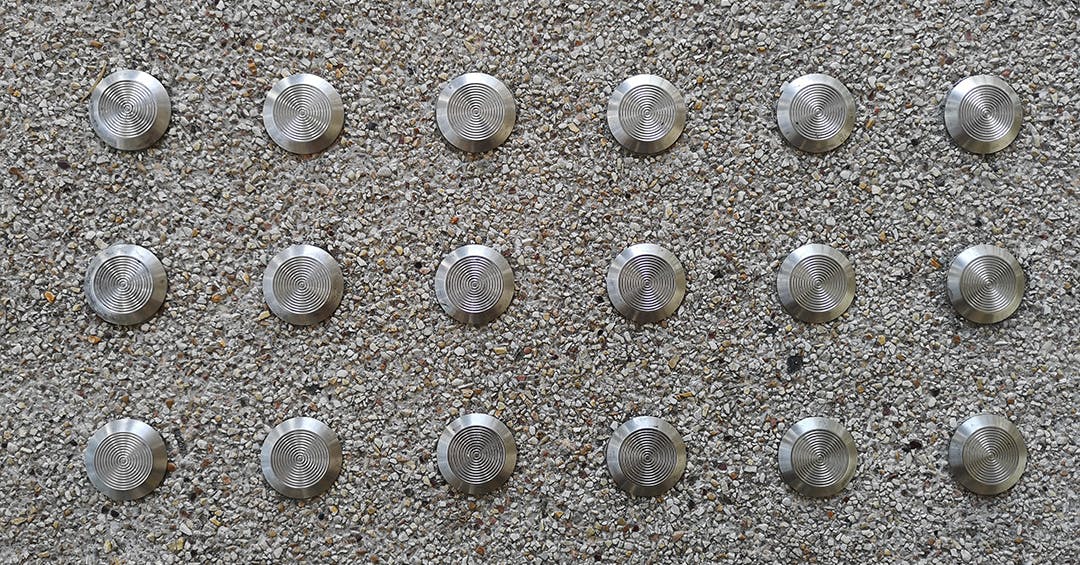 Stainless steel tactile handrail fittings arranged in a grid pattern on textured concrete, providing safe navigation for visually impaired pedestrians.