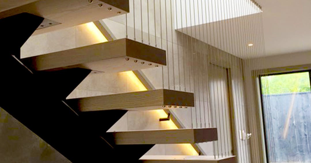 Floating staircase featuring wire balustrading with vertical cables and timber treads, designed with subtle lighting to create a sleek and modern interior.