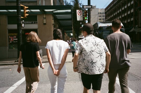 View from behind a group of people walk across street on a sunny day