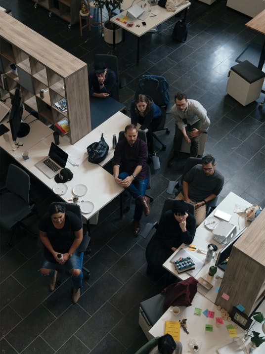 Bird's eye view shot of seven seated people during a meeting looking intently in the same direction