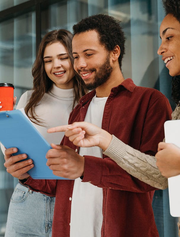 3 pessoas observando um tablet. Estão sorrindo, um homem e duas mulheres