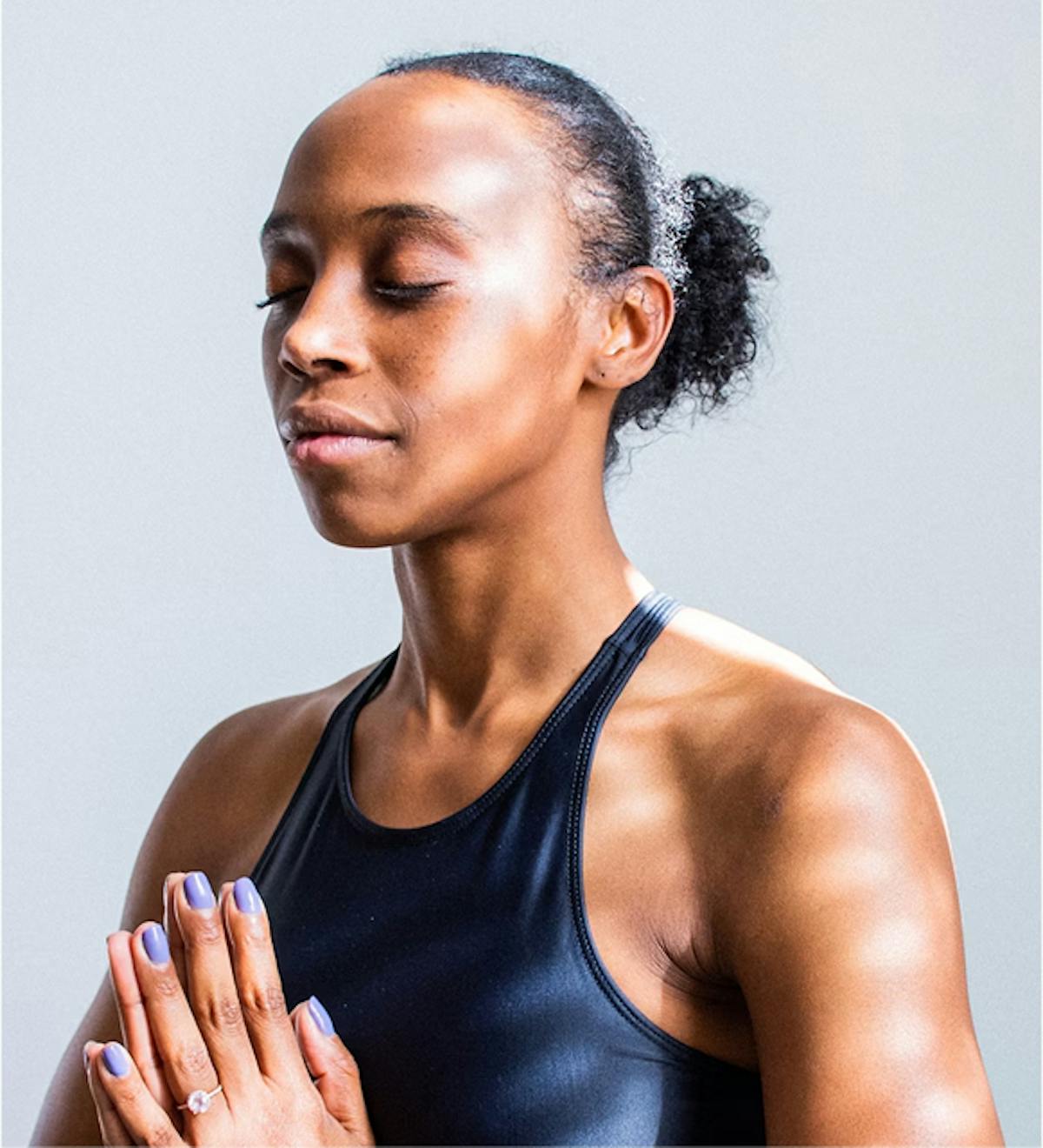 Mulher meditando e feliz. A mulher é uma afro-descendente e está com uma camiseta regata azul escura.