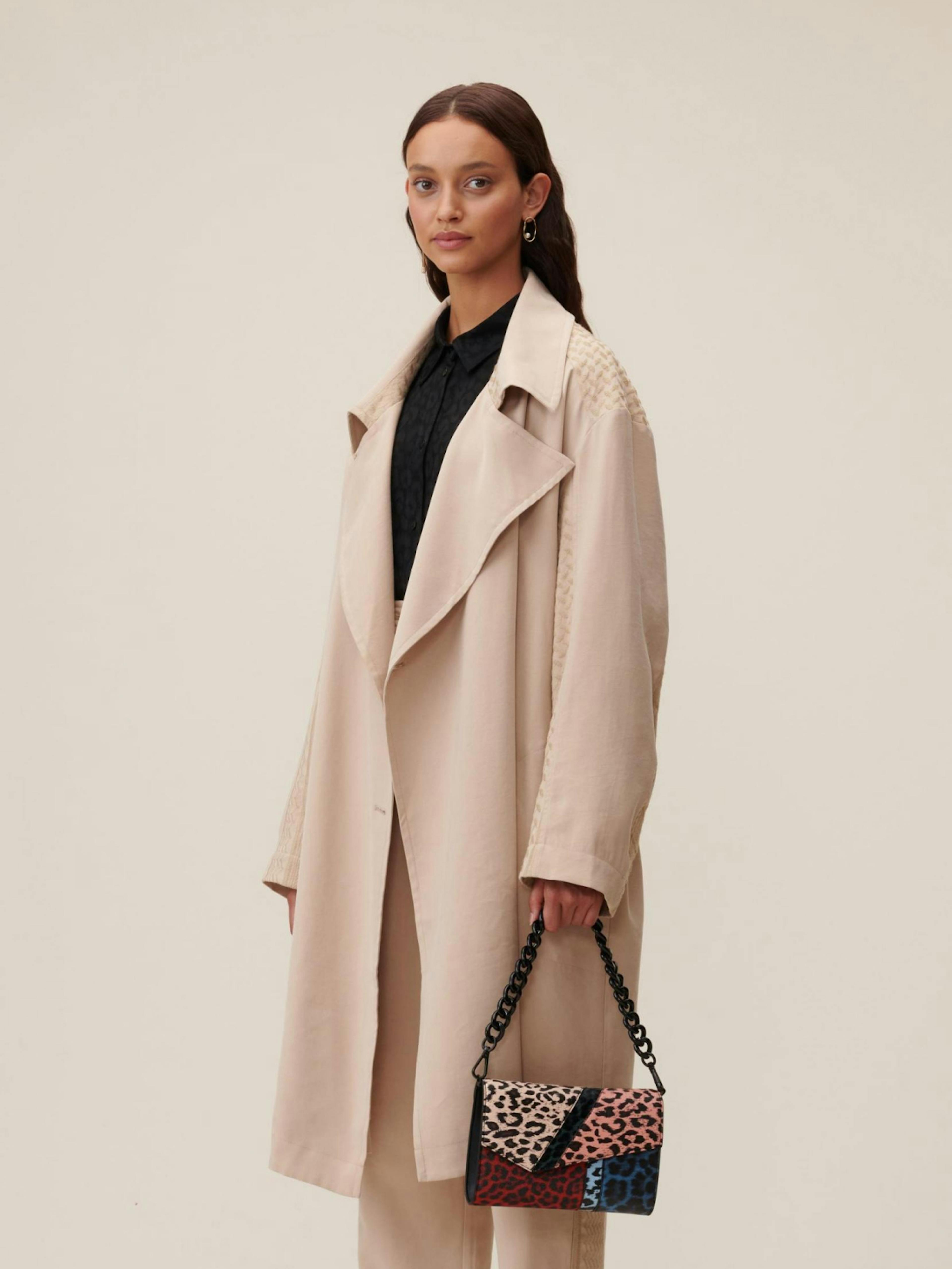 lala Berlin – Brand Design, E-Commerce, Experience Design "Celebrating Differences": Photo showing a woman wearing a beige trench coat and holding a colorful patchwork bag x HY.AM Studios