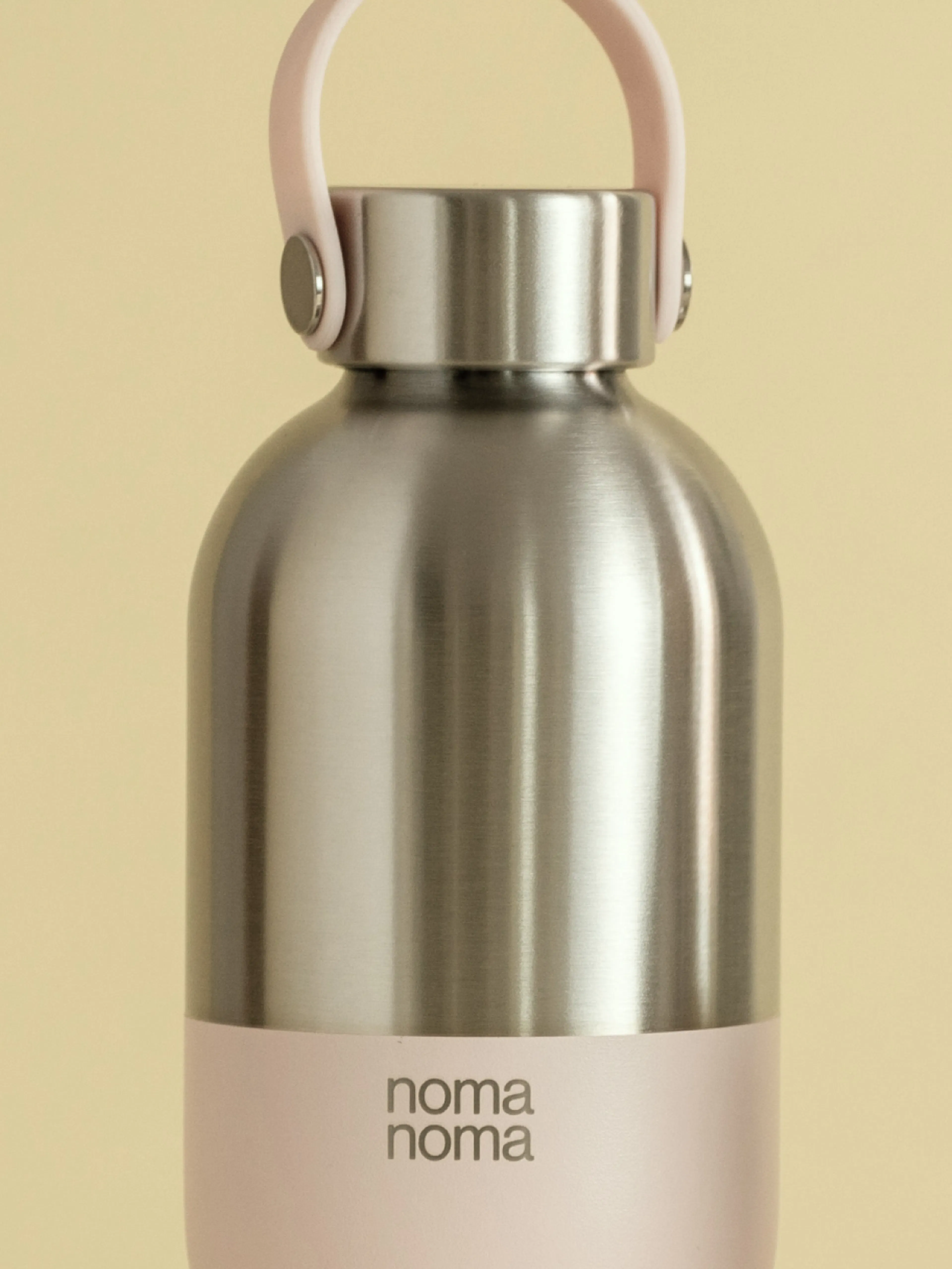 noma noma – Brand Design, E-Commerce, Experience Design "A conscious companion becomes a personal style icon": Mockup showing a brushed metal water bottle with a pink accent band and handle, featuring the noma noma logo x HY.AM Studios
