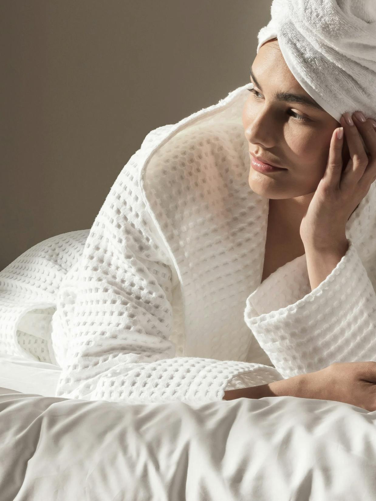 Möve – Brand Design, E-Commerce, Experience Design "A contemporary shopping experience for home textiles": Photo showing a woman wearing a white waffle-knit bathrobe and towel, resting on a bed x HY.AM Studios