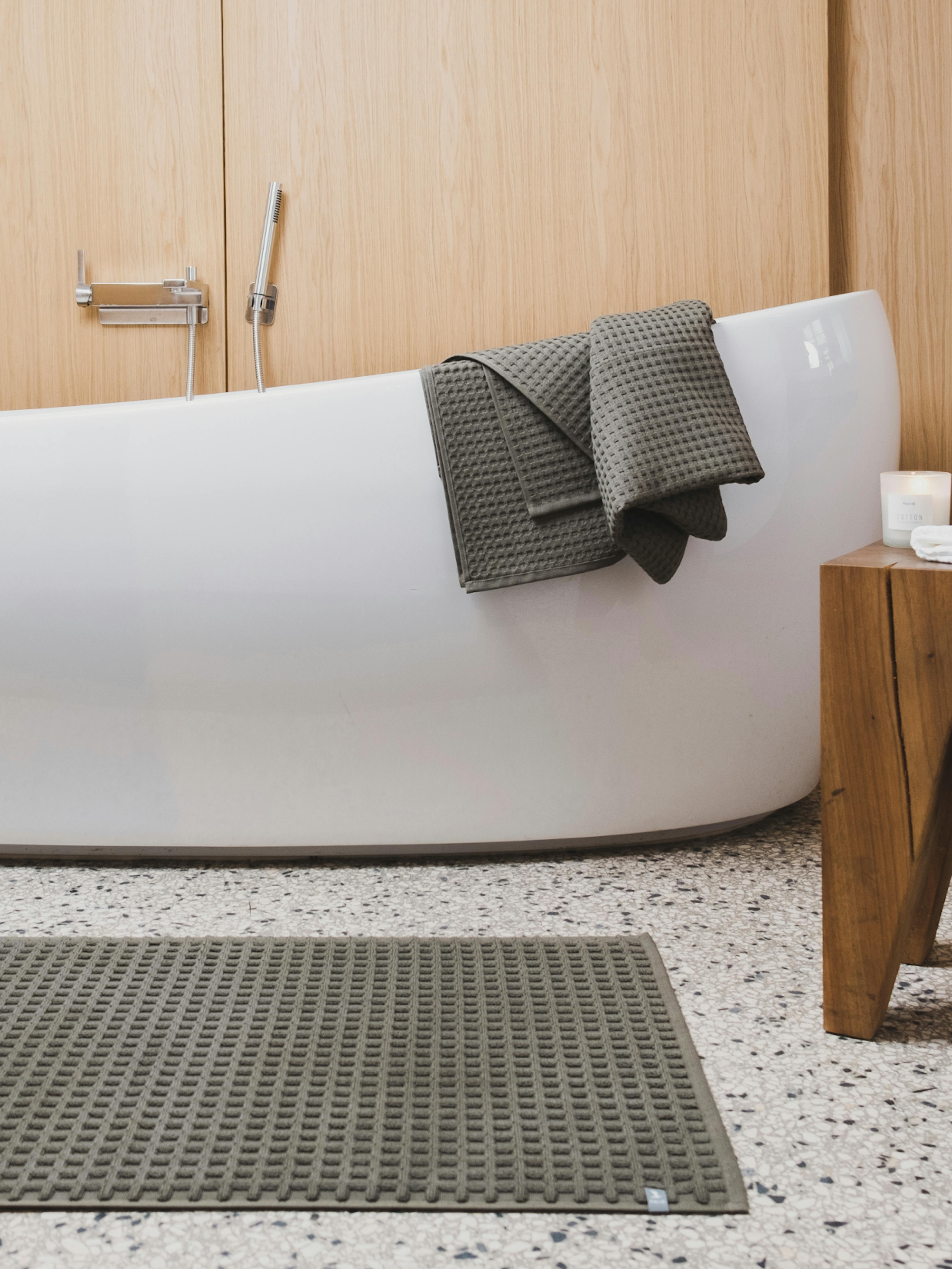 Möve – Brand Design, E-Commerce, Experience Design "A contemporary shopping experience for home textiles": Photo showing a modern bathroom with a white bathtub, grey waffle-weave towels, and a matching bath mat x HY.AM Studios