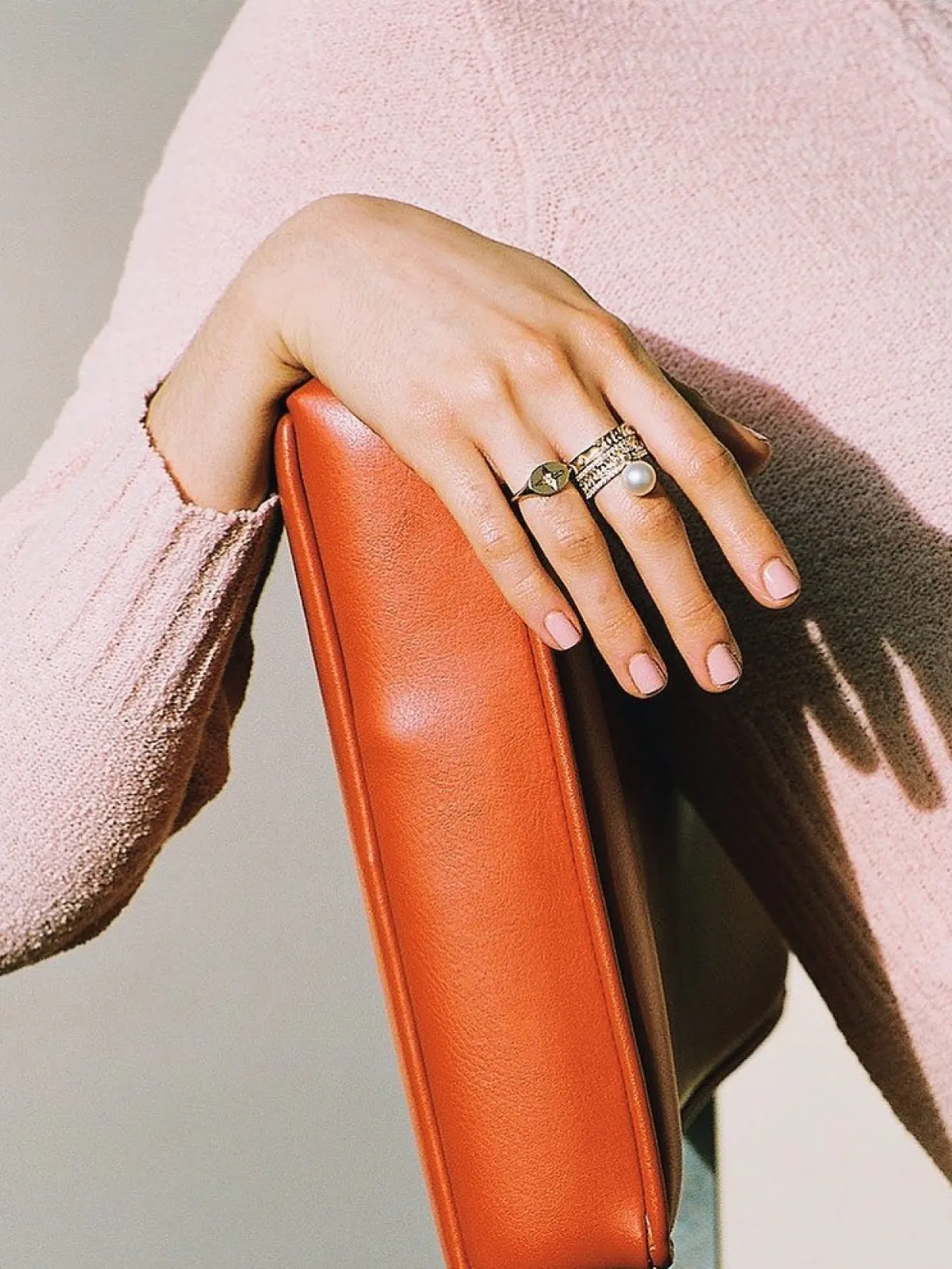 Marlo Laz – Brand Design, E-Commerce, Experience Design "A luxury shopping voyage": Photo showing a hand with rings resting on an orange surface, wearing a pink sweater x HY.AM Studios