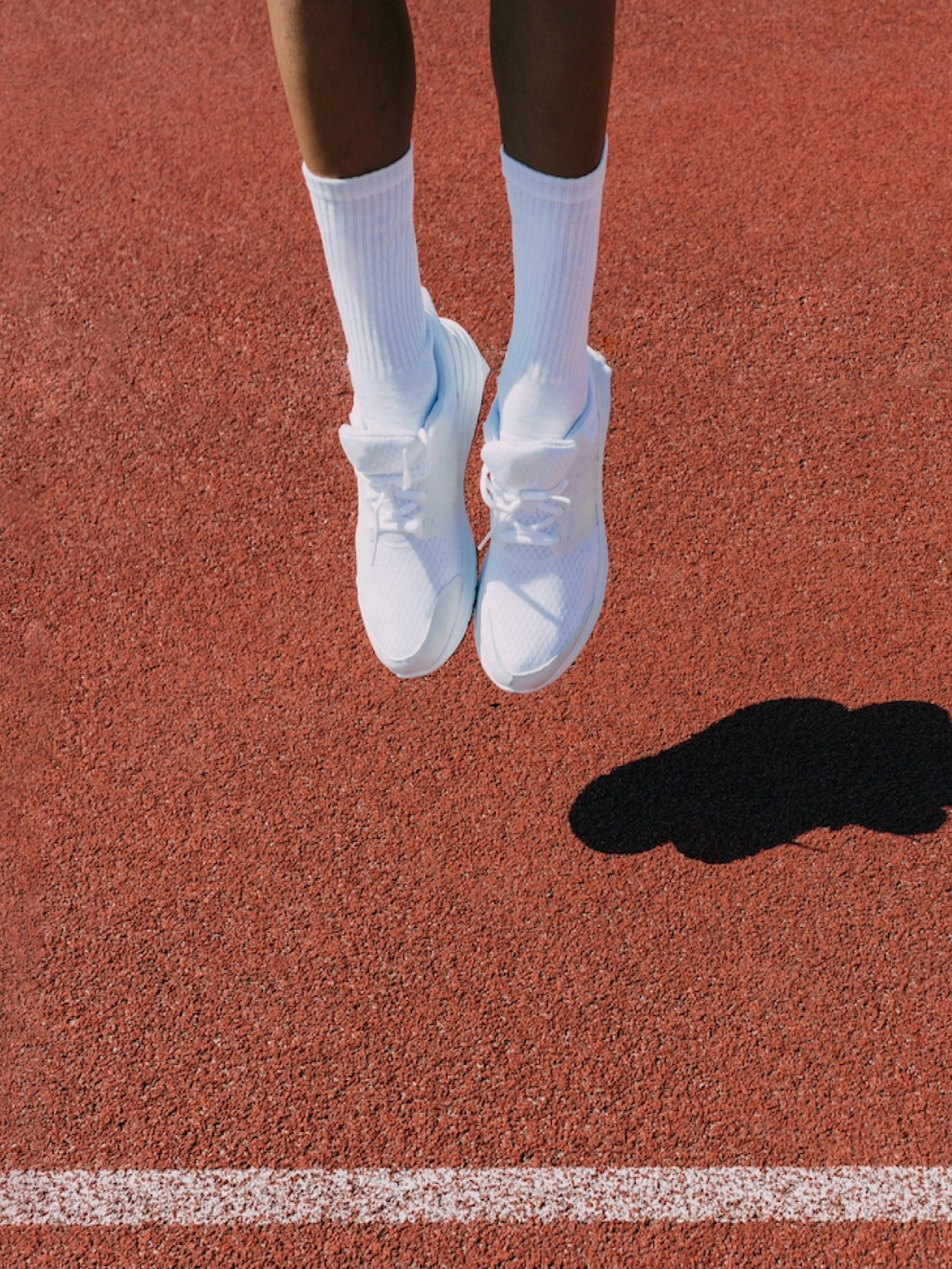 Berlin Brands Group – Brand Design "Berlin Brands Group": Photo showing a person's legs wearing white socks and white sneakers, jumping on a red running track x HY.AM Studios