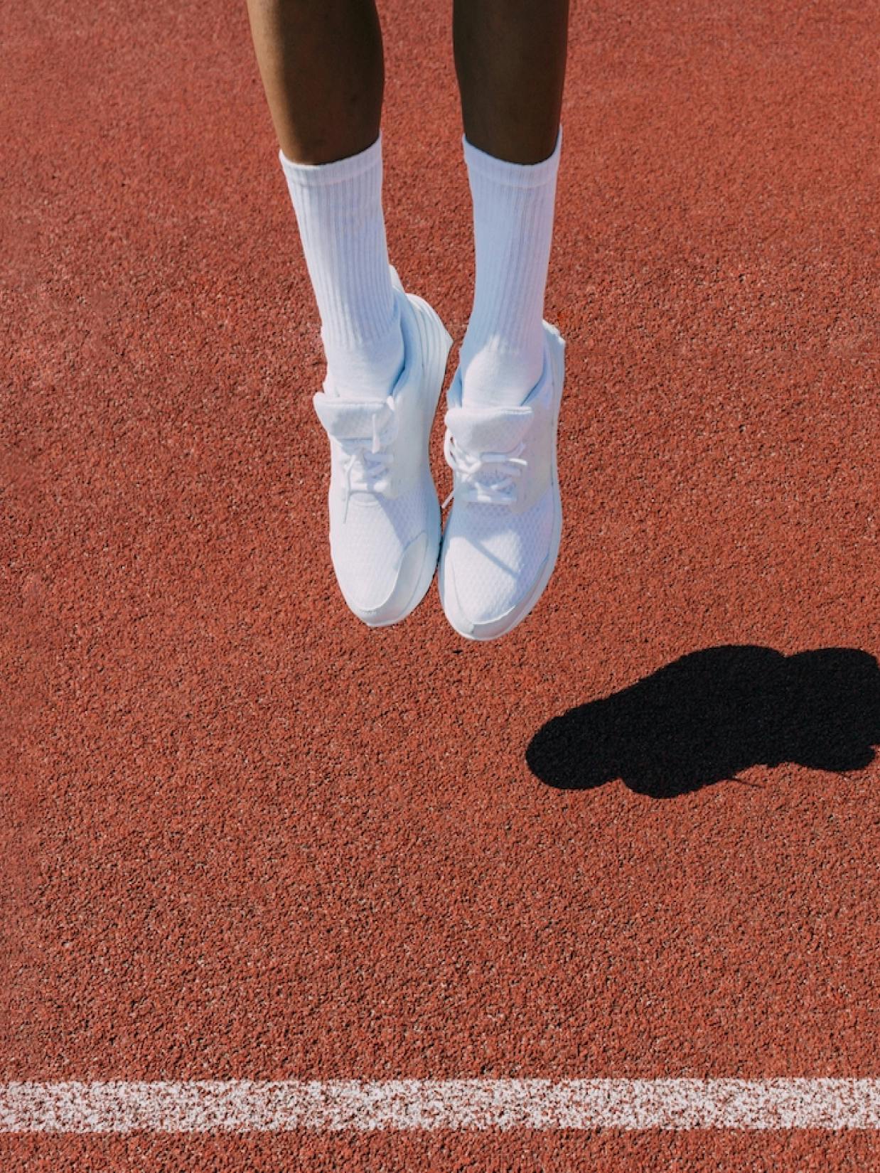 Berlin Brands Group – Brand Design "Berlin Brands Group": Photo showing a person's legs wearing white socks and white sneakers, jumping on a red running track x HY.AM Studios