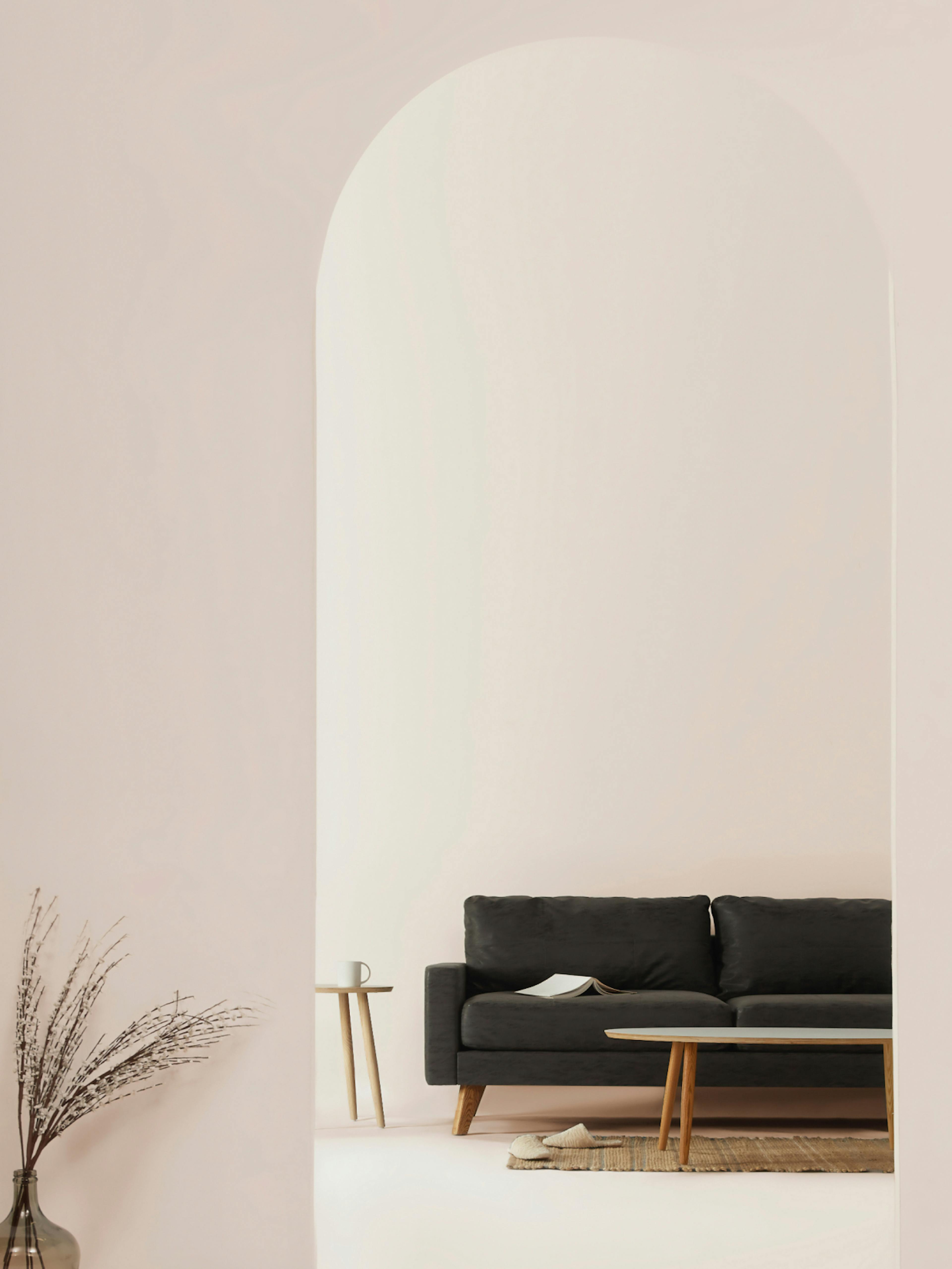 Home24 – Brand Design, E-Commerce, Experience Design "Europe's online store for furniture": Photo showing a dark grey sofa with a book on it, a small side table with a mug, and a vase with dried branches in a minimalist interior x HY.AM Studios