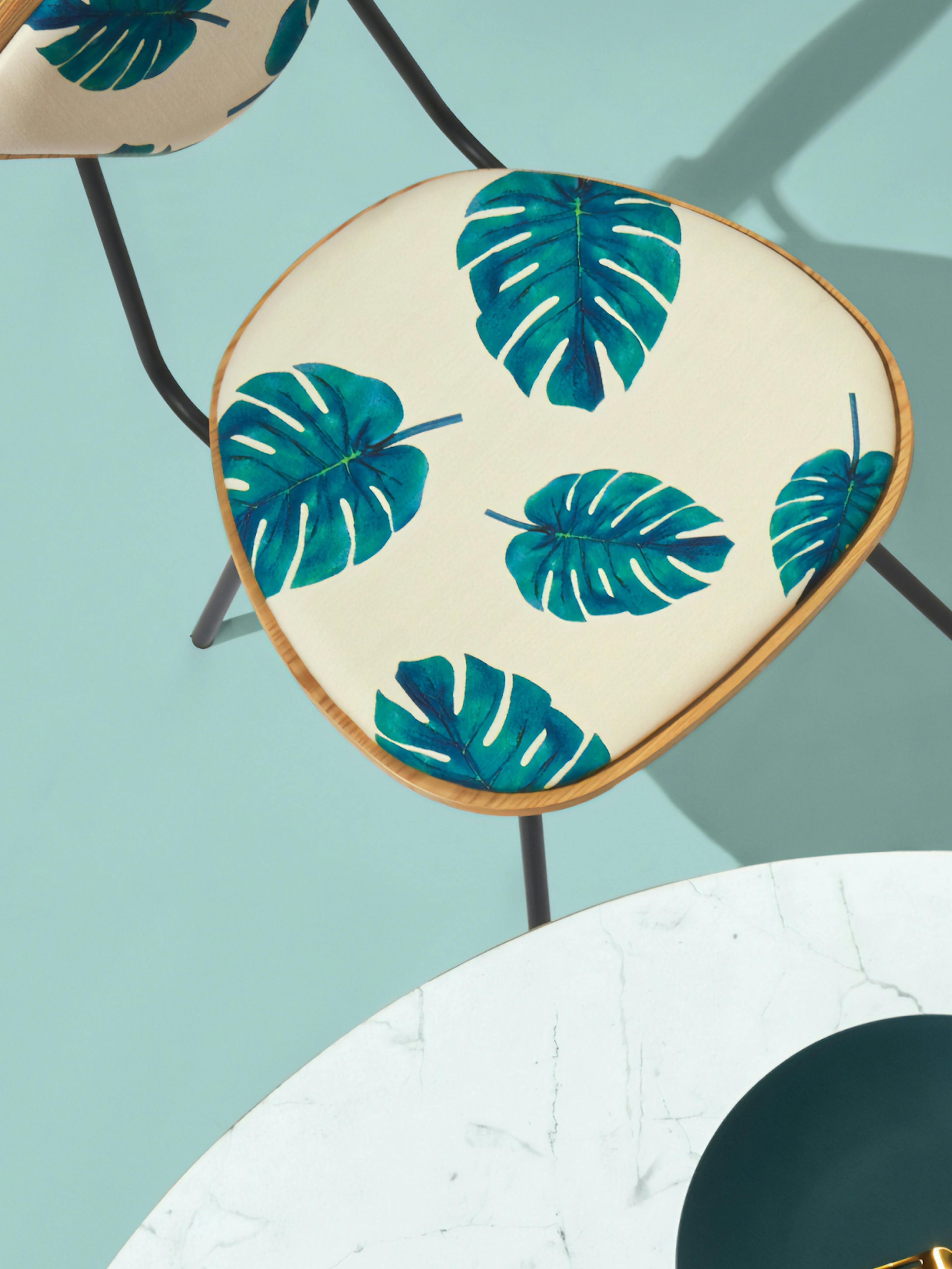 Home24 – Brand Design, E-Commerce, Experience Design "Europe's online store for furniture": Photo showing a chair with a cream-colored seat featuring a pattern of teal monstera leaves x HY.AM Studios