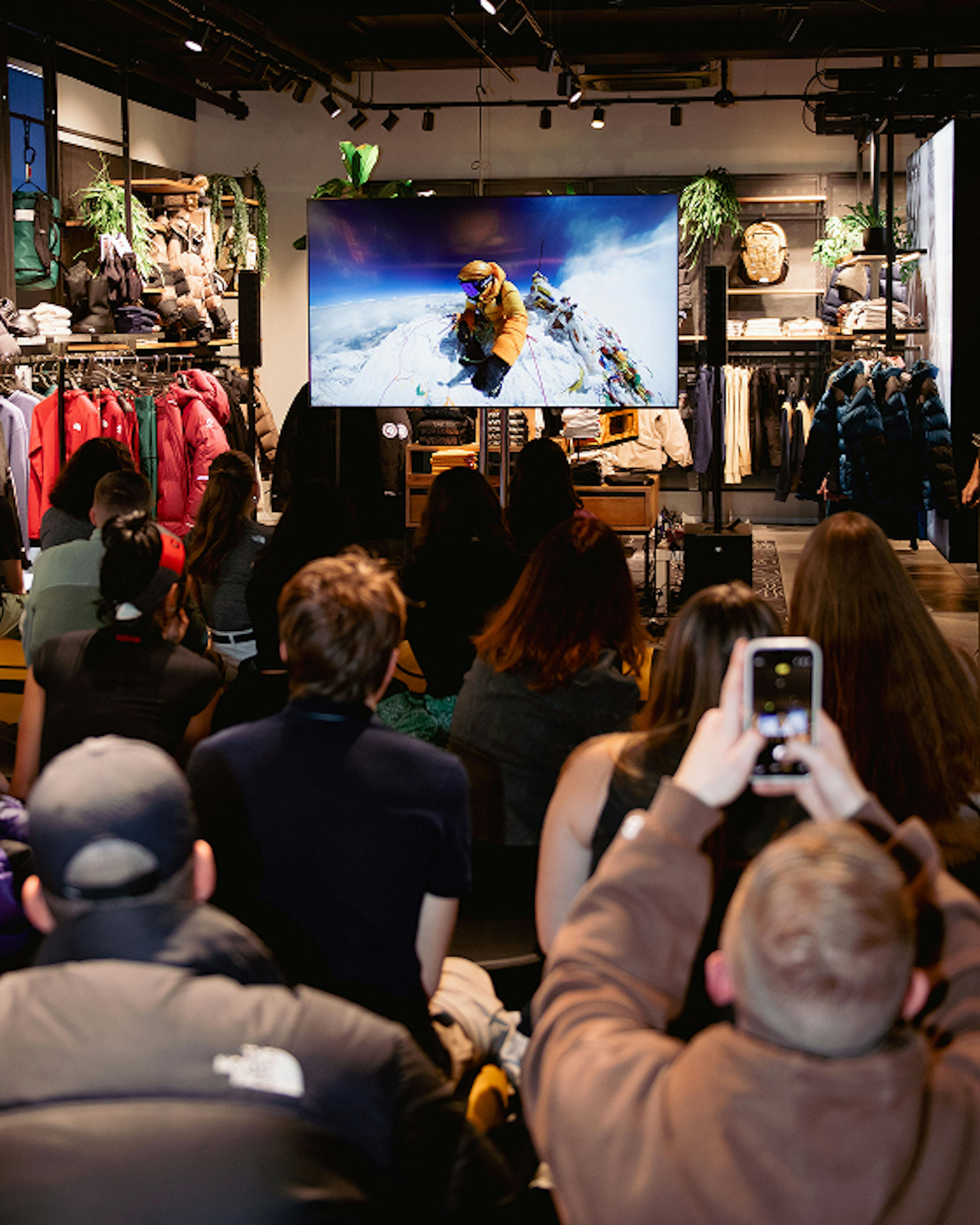 The North Face – Brand Activation "Summit Series Brand Activation": Photo showing a screen displaying a mountaineer on a snowy peak, with an audience watching in a store setting x HY.AM Studios