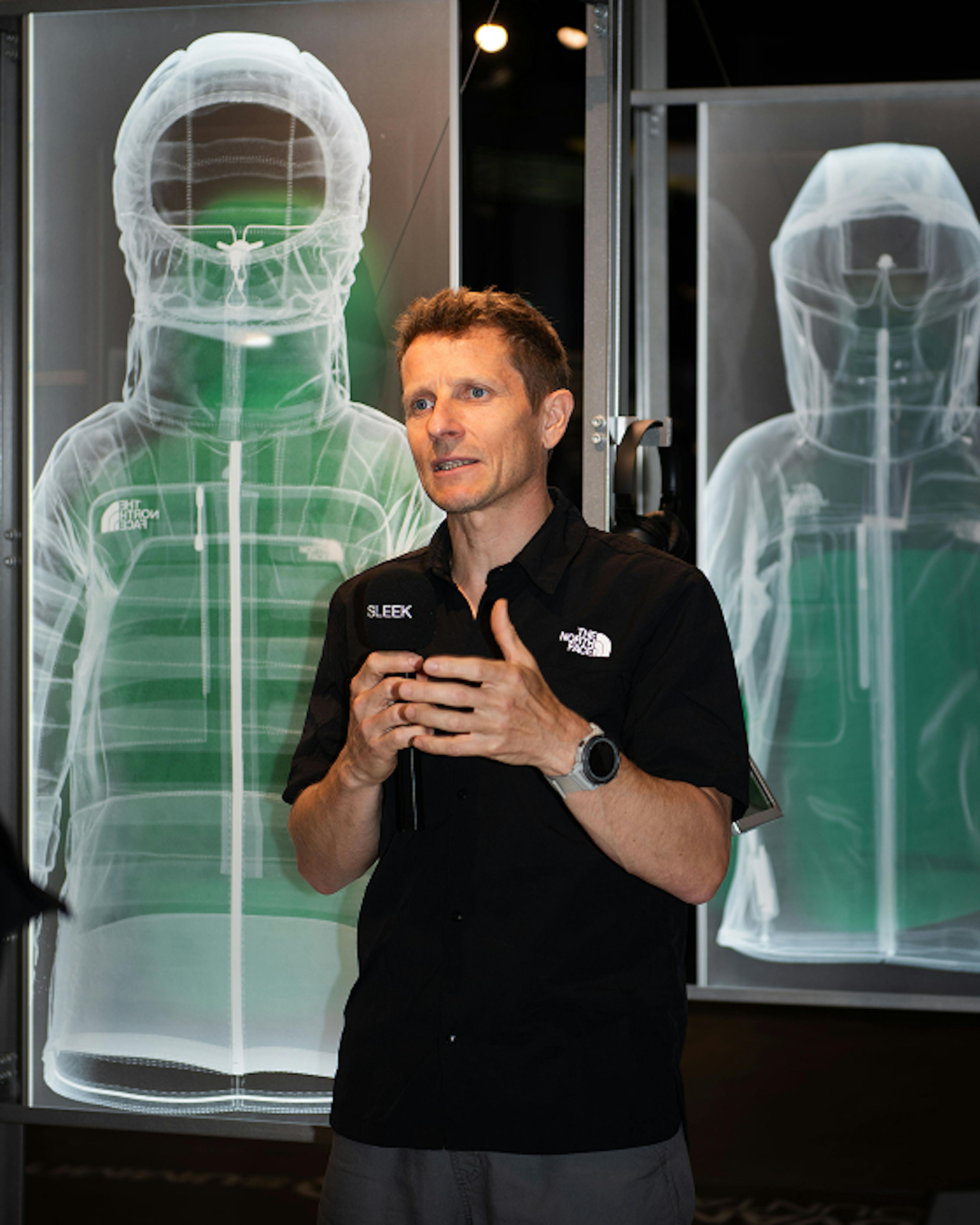 The North Face – Brand Activation "Summit Series Brand Activation": Photo showing a man in a black shirt presenting in front of a transparent display of a North Face jacket x HY.AM Studios