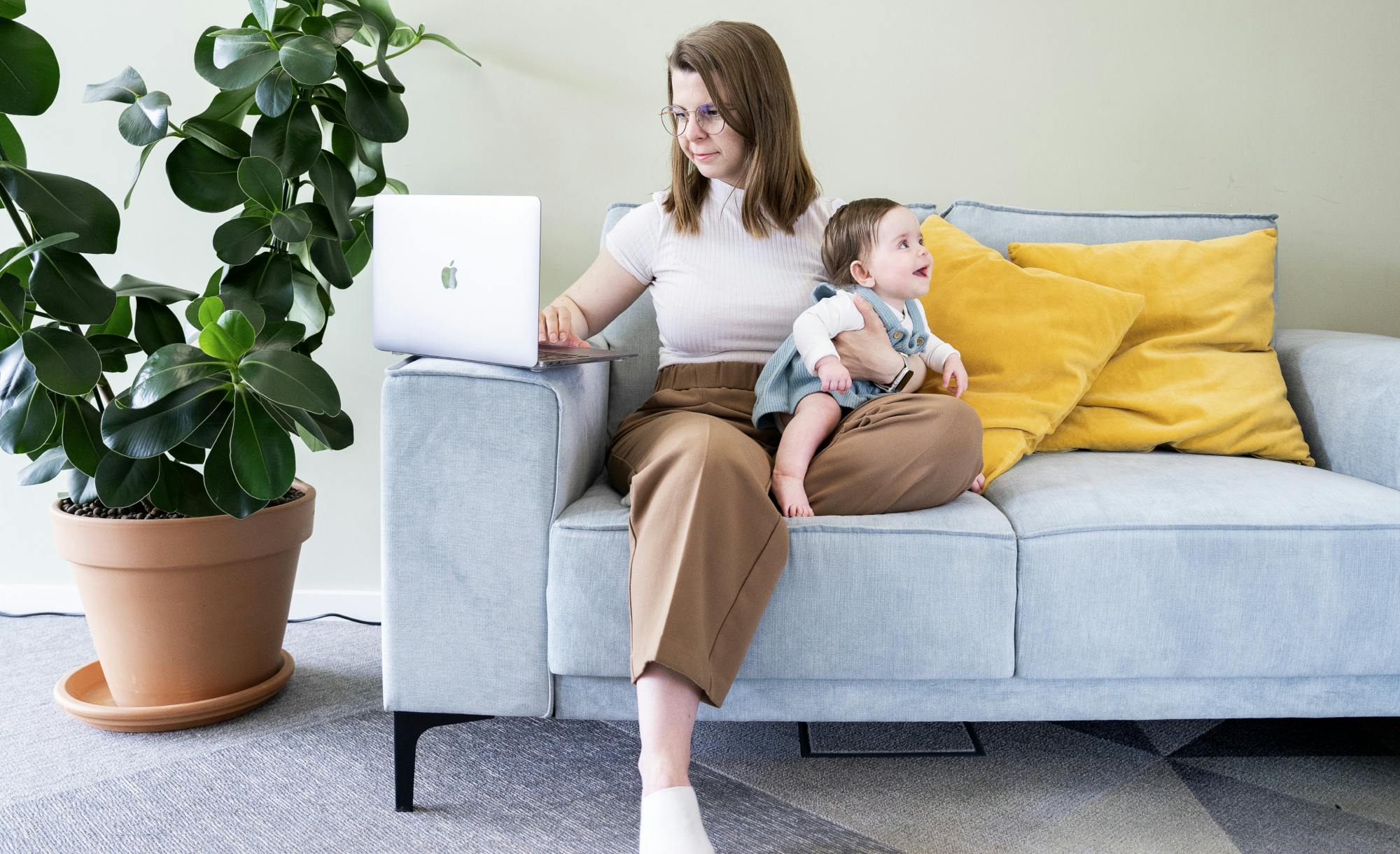 developer sitting on a sofa with a baby in her lap and a laptop on an armrest