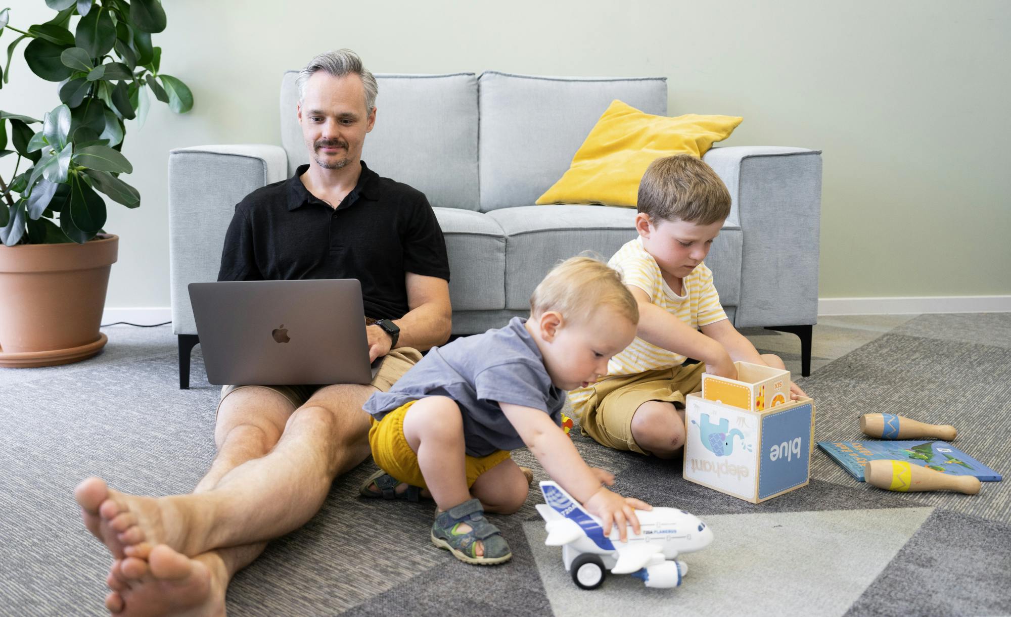 solution architect with a laptop on his lap sitting on the floor next to his children