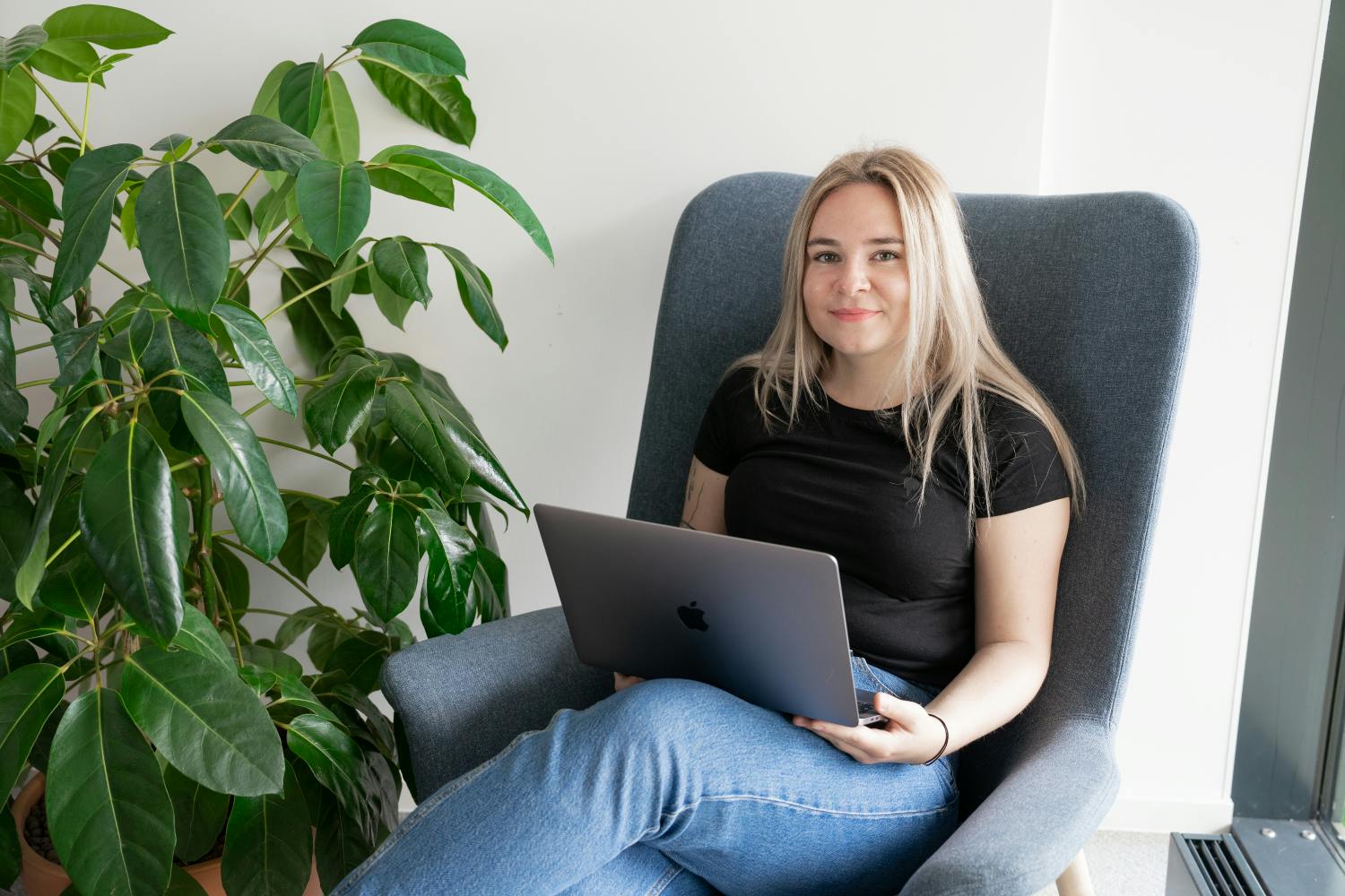 business support specialist posing with a laptop next to a plant