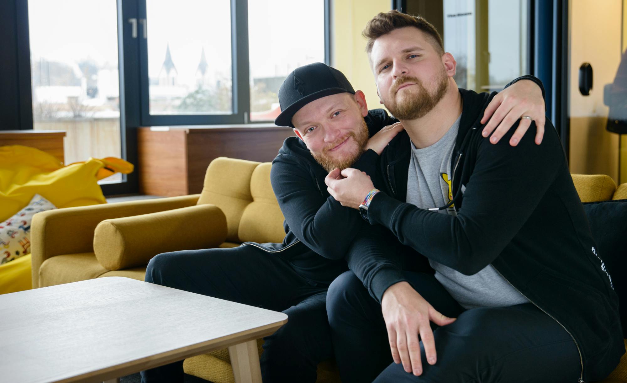 The two co-founders sitting on a couch, one with his arm around the other, in a friendly, relaxed pose.