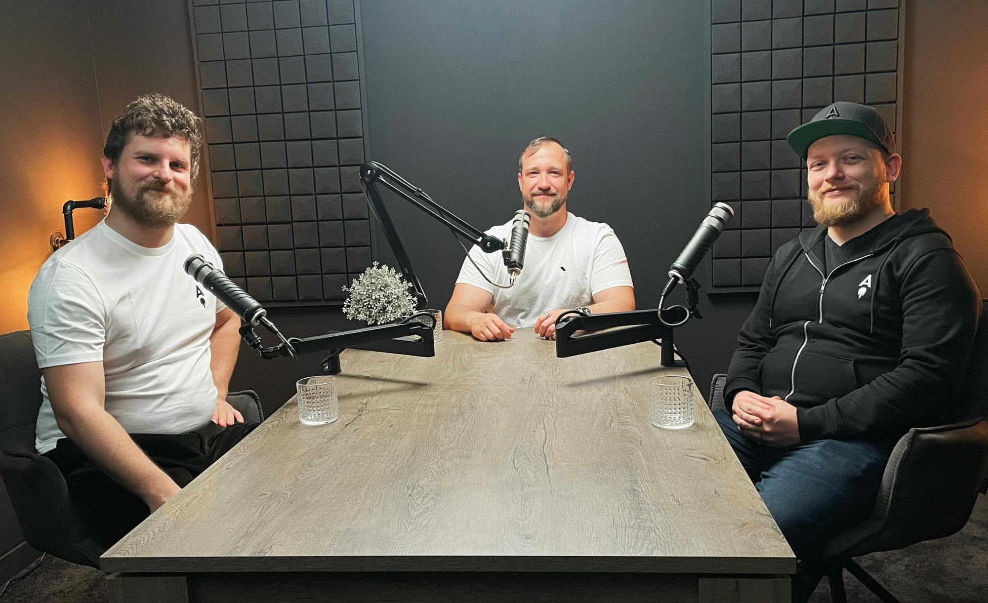 The two co-founders and the moderator sitting at a podcast table with microphones, engaging in a discussion.