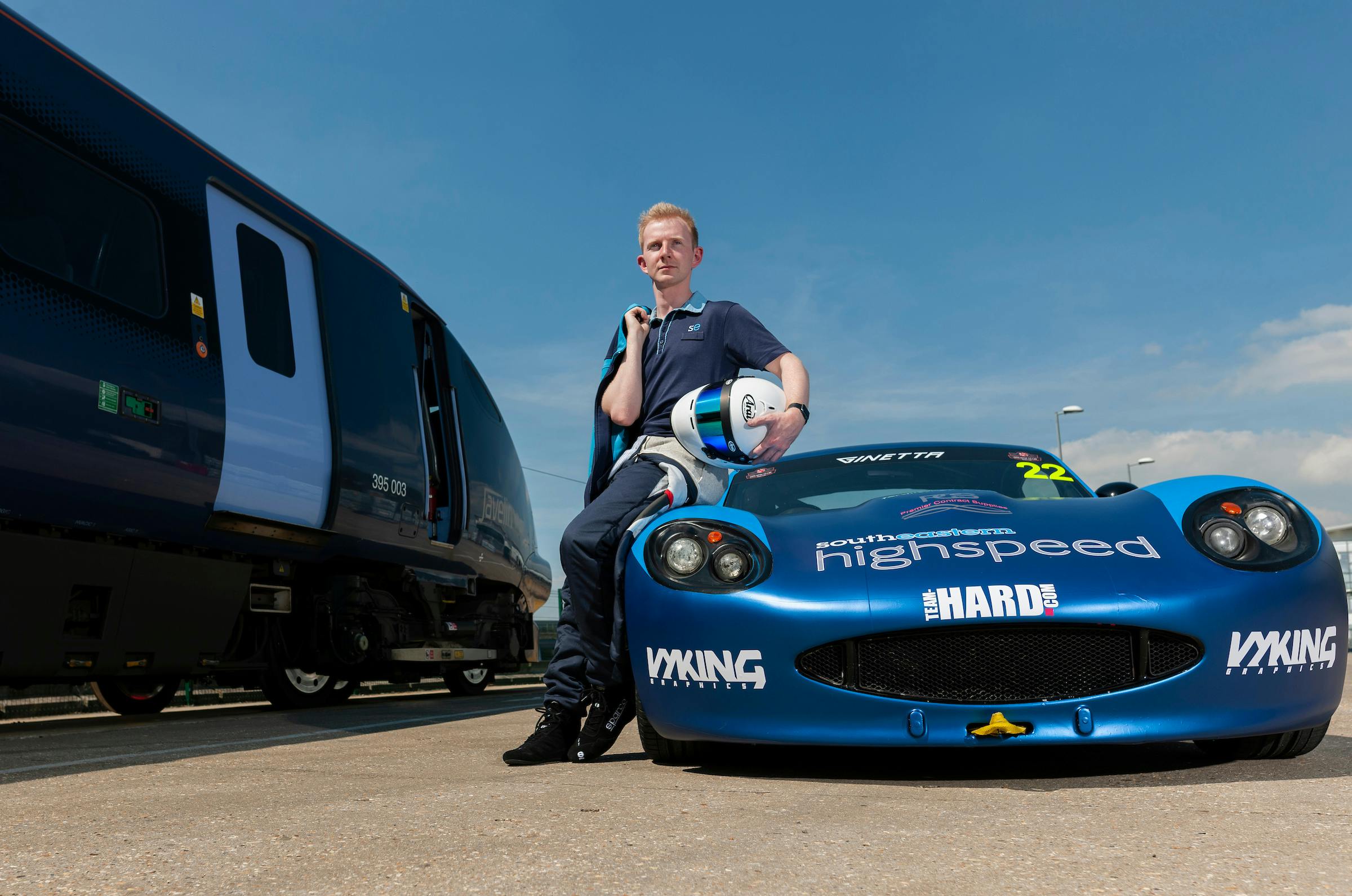 Toby Trice sitting on the hood of his racing car, parked adjacent to a train.