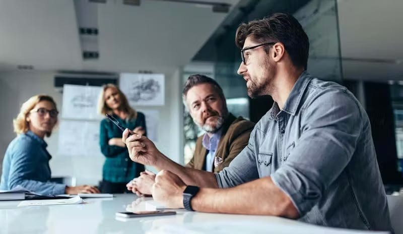 Image shows 4 people in a meeting room.