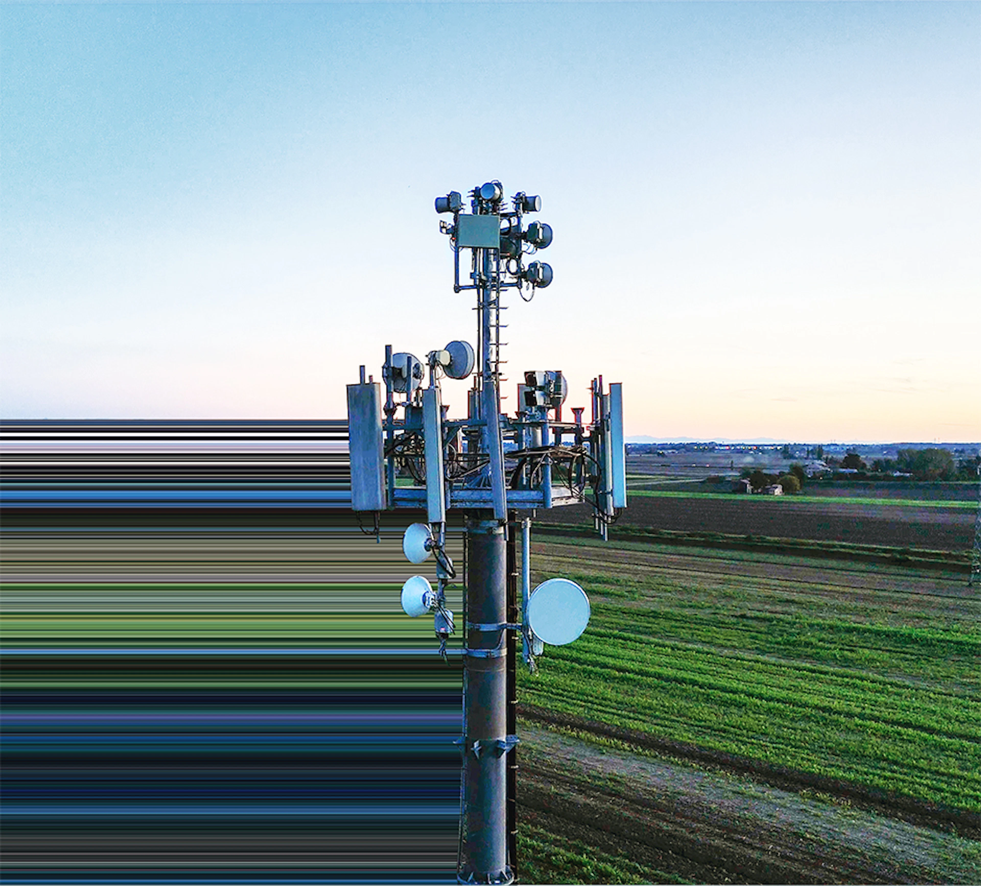 Telecommunications cell tower rising above farmland at sunset