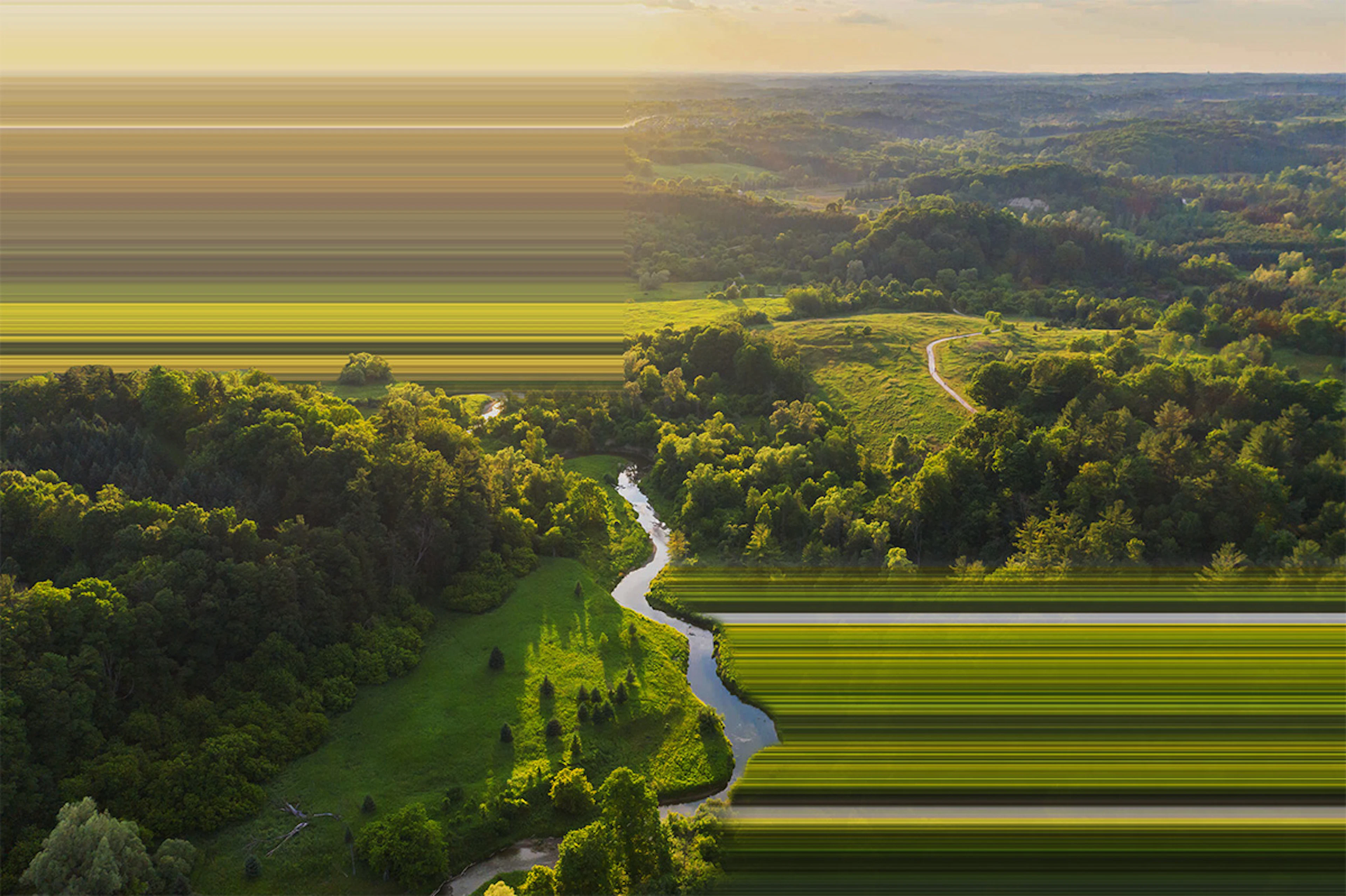 River through grass and tree covered farmland at sunset