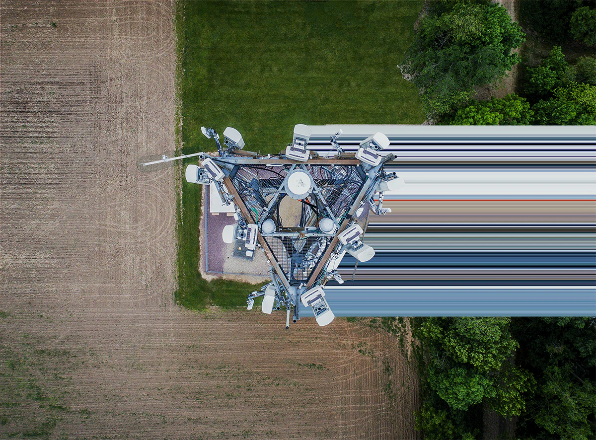 Aerial top-down view of a telecom cell tower and its equipment beside farmland and trees