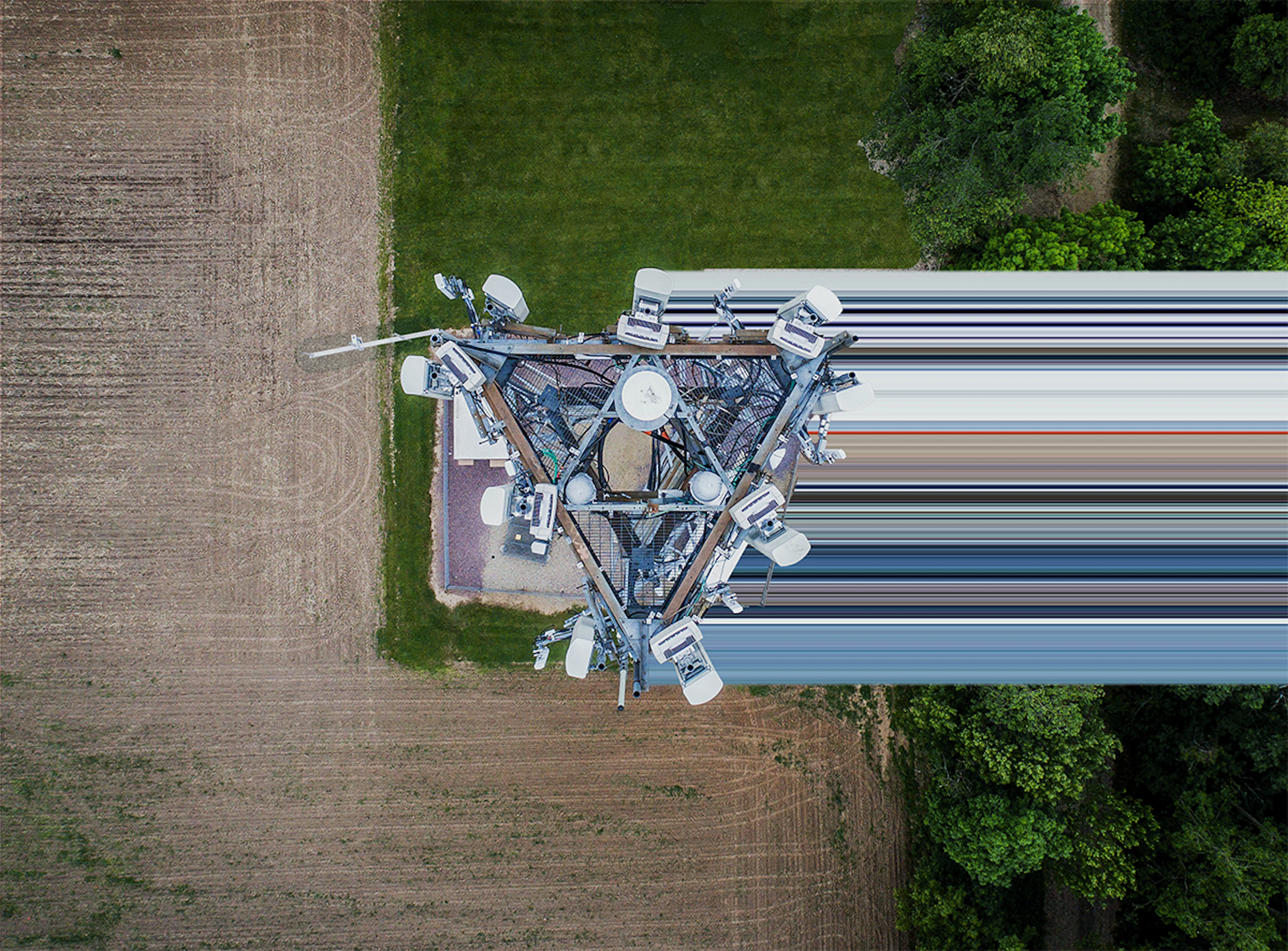 Aerial top-down view of a telecom cell tower and its equipment beside farmland and trees