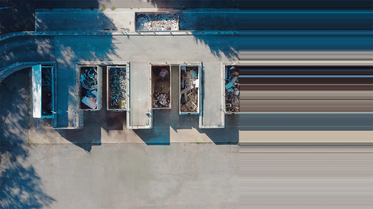 Aerial view of a row of large waste dumpsters lined up on pavement road