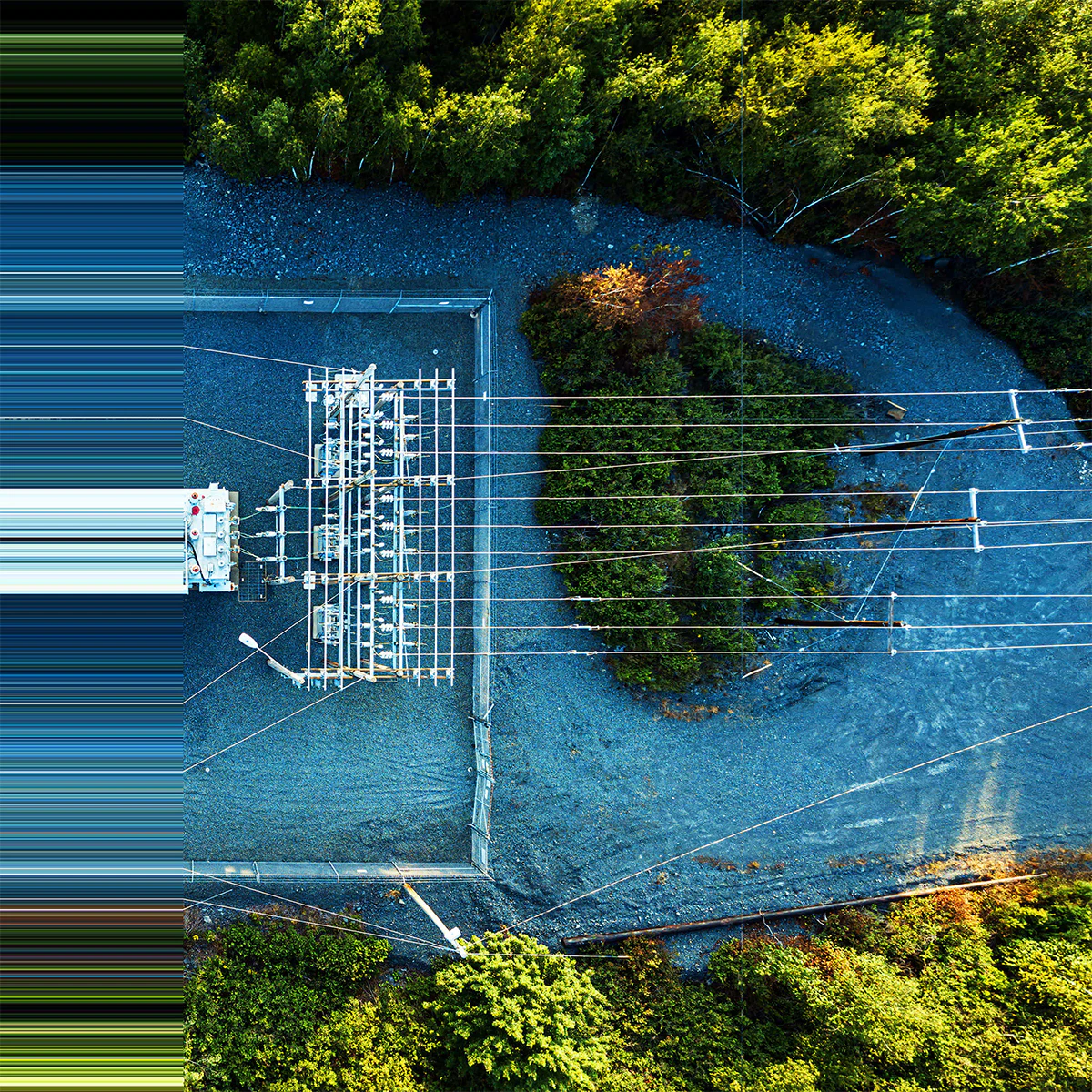 Aerial view of an electrical substation with transformers and equipment, surrounded by green trees