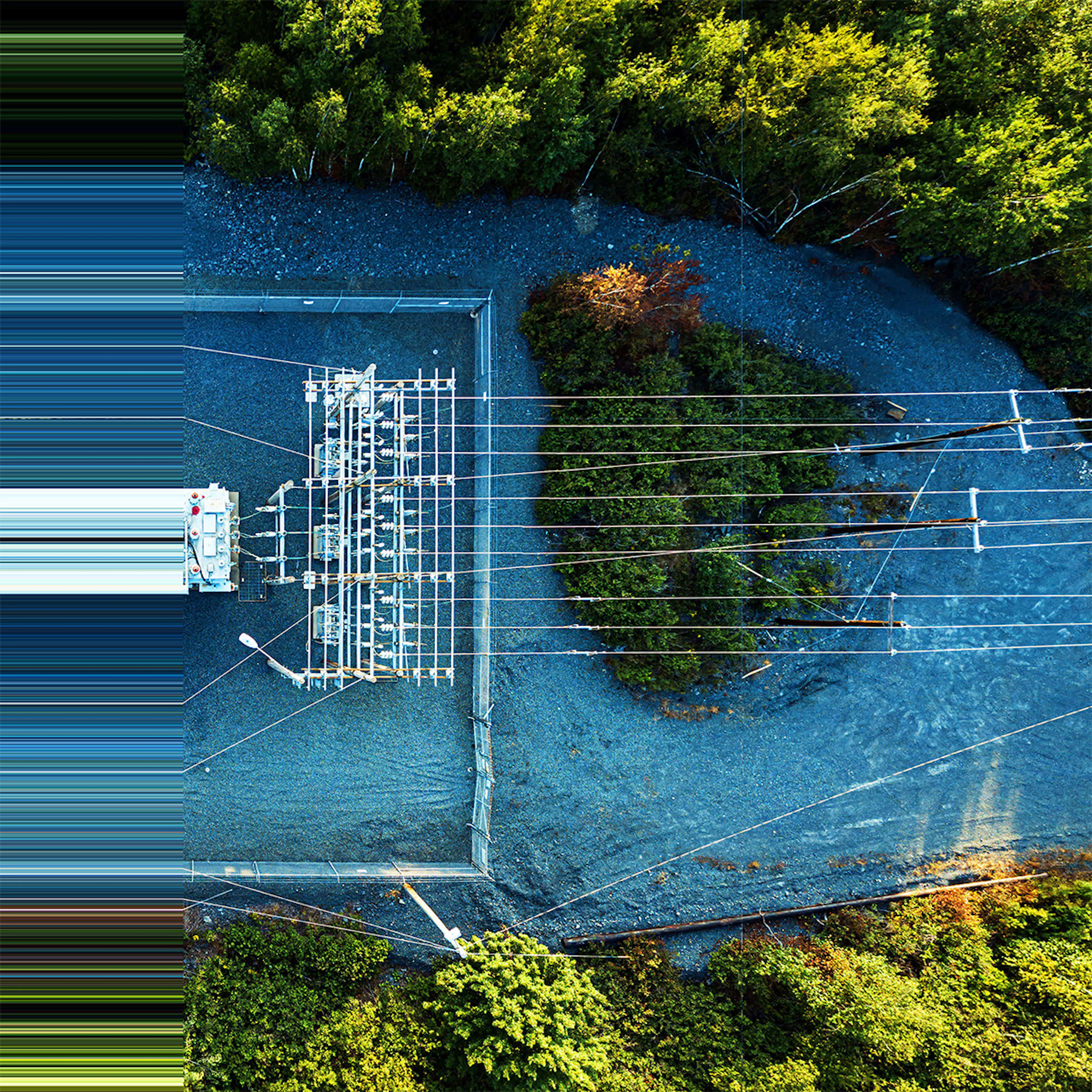 Aerial view of an electrical substation with transformers and equipment, surrounded by green trees