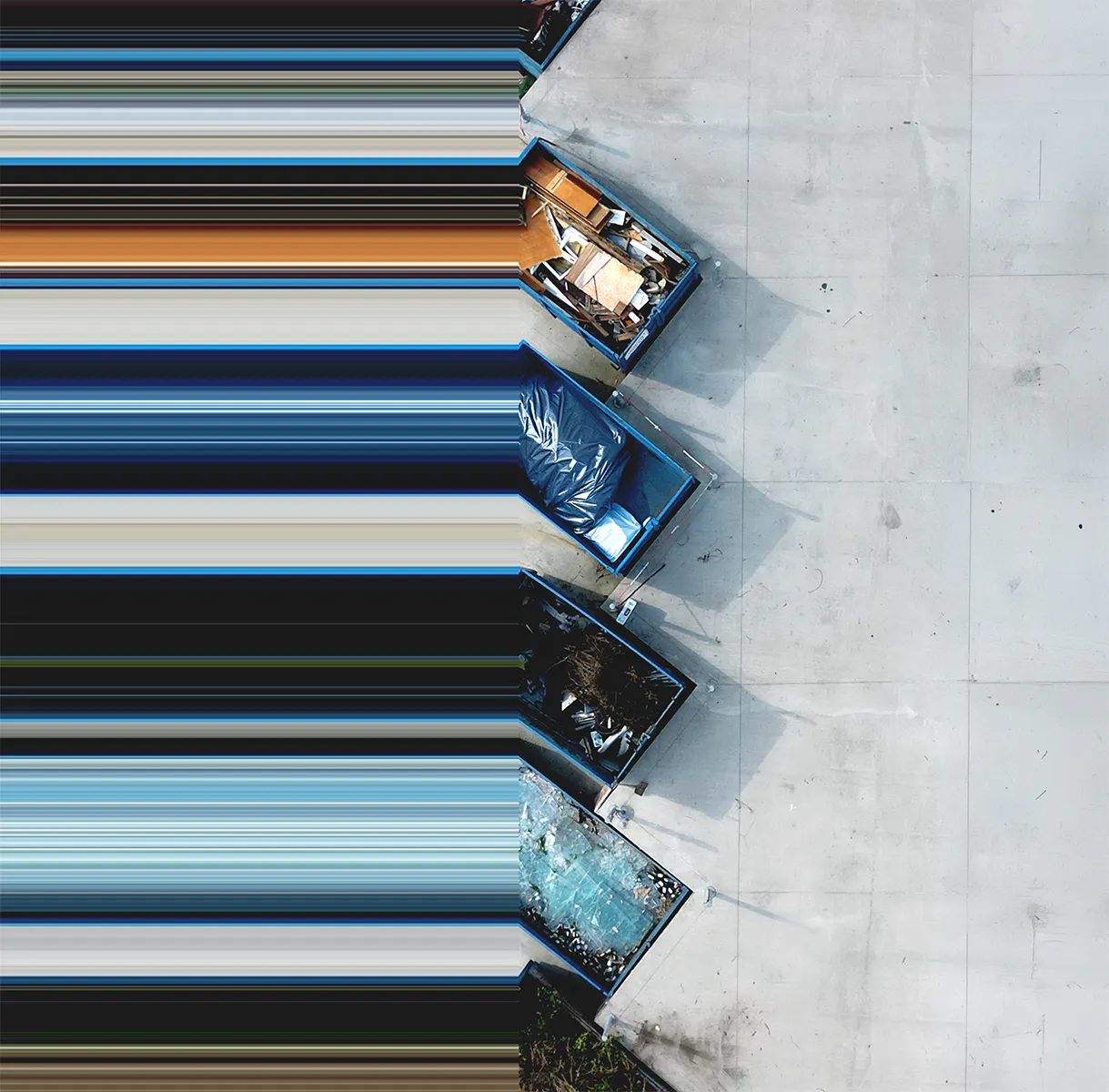 Aerial view of a row of large waste dumpsters lined up on pavement