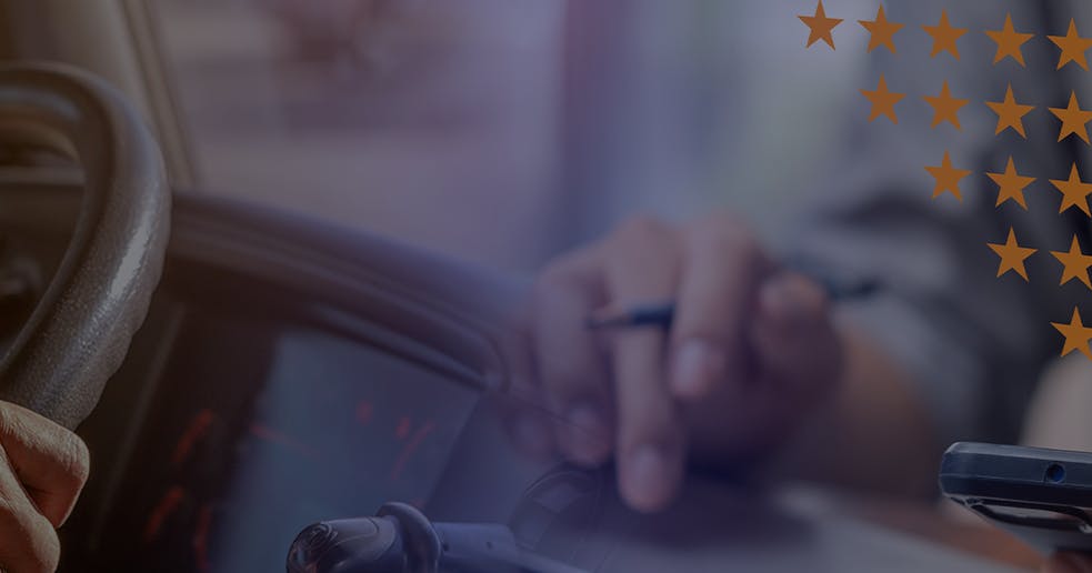 Mãos de um motorista segurando o volante de um caminhão, enquanto no lado direito aparecem ícones digitais de avaliação com estrelas, checklist de motoristas e um selo de premiação dourado, simbolizando ranqueamento e reconhecimento de desempenho.
