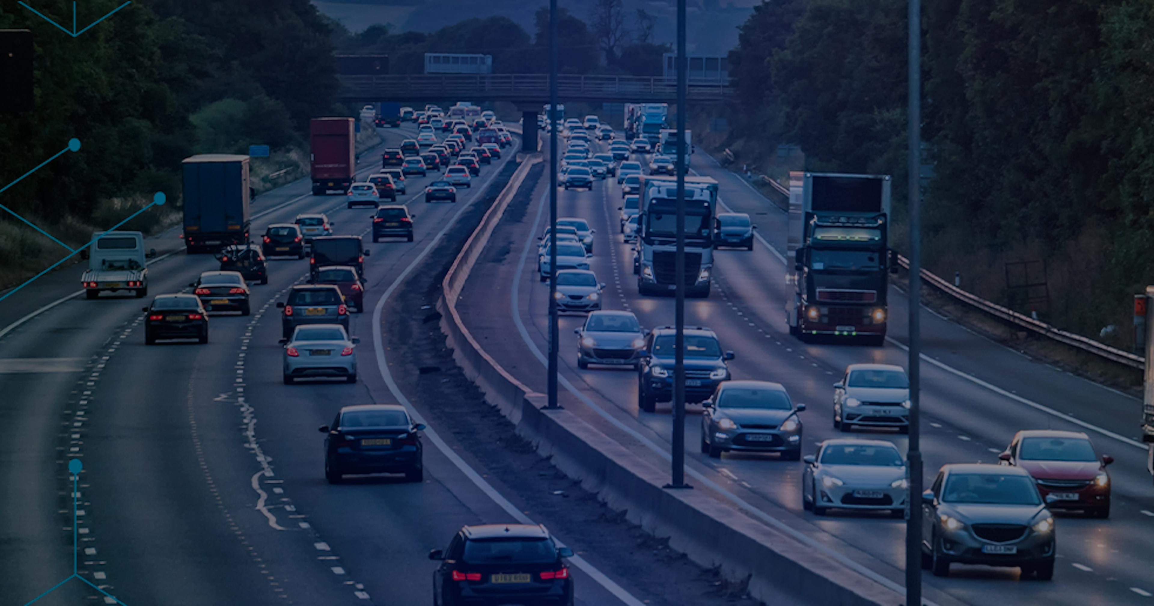 Rodovia movimentada com fluxo intenso de carros e caminhões em várias faixas, cercada por árvores, com sobreposição de gráficos em forma de hexágonos azuis que remetem à tecnologia e conectividade.