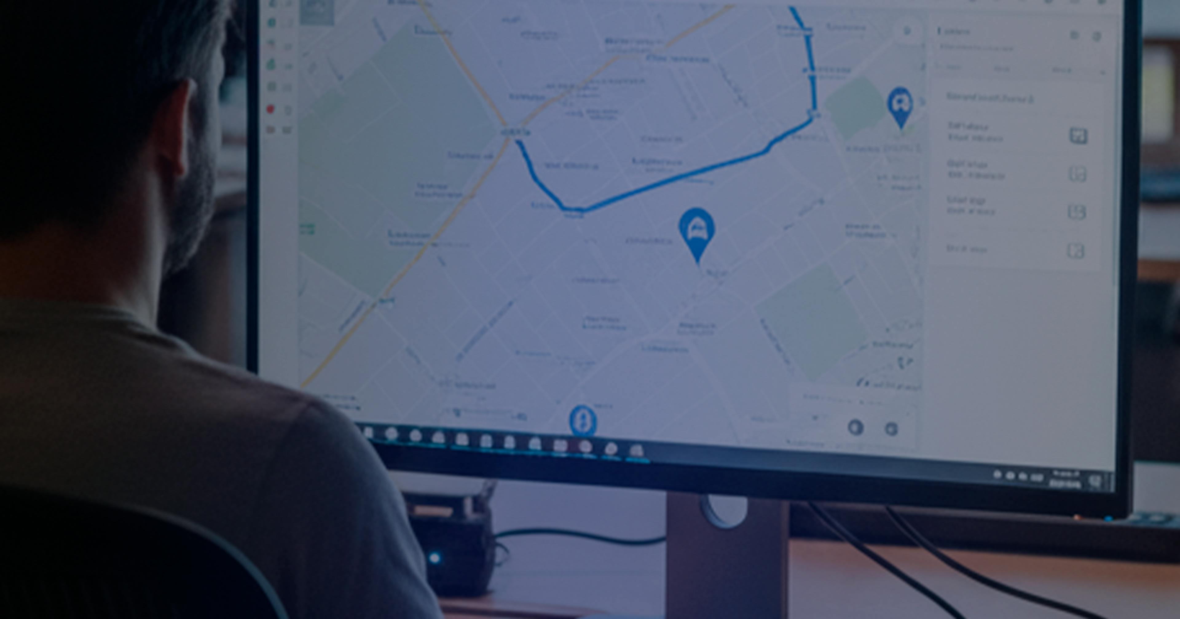 Profissional em frente a um monitor exibindo um mapa com rotas e pontos de localização, em um ambiente de escritório moderno, representando o monitoramento e gestão de frotas em tempo real