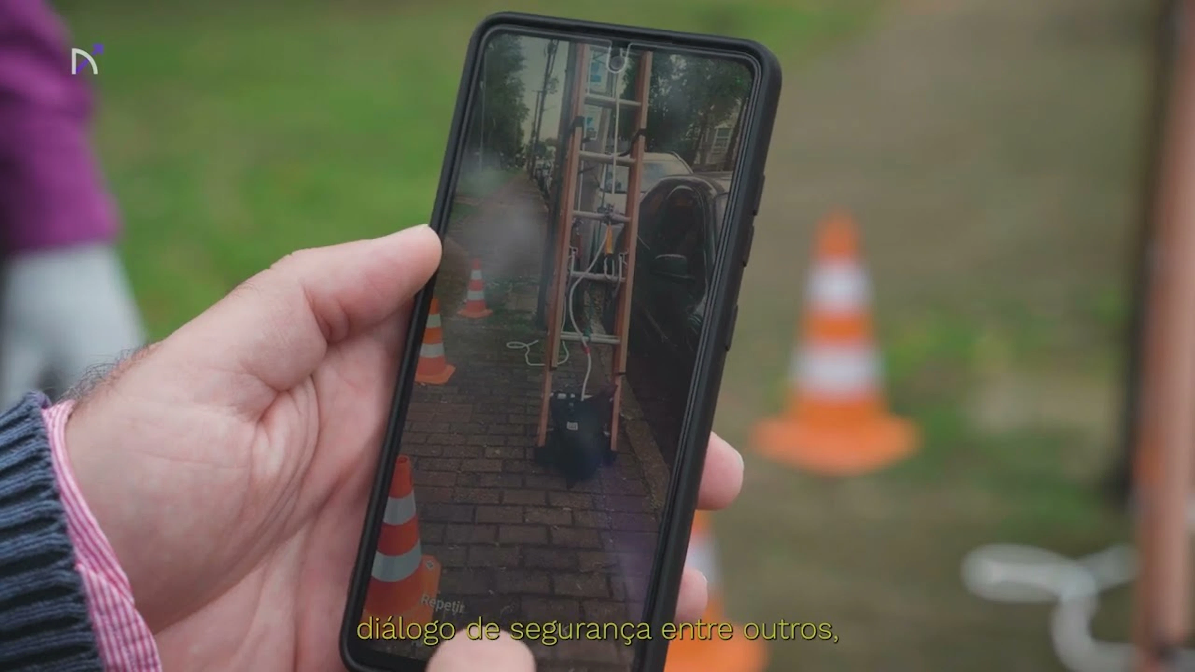 Mão segurando um celular que mostra uma escada e cones de sinalização numa calçada, capa do vídeo da plataforma Arkium