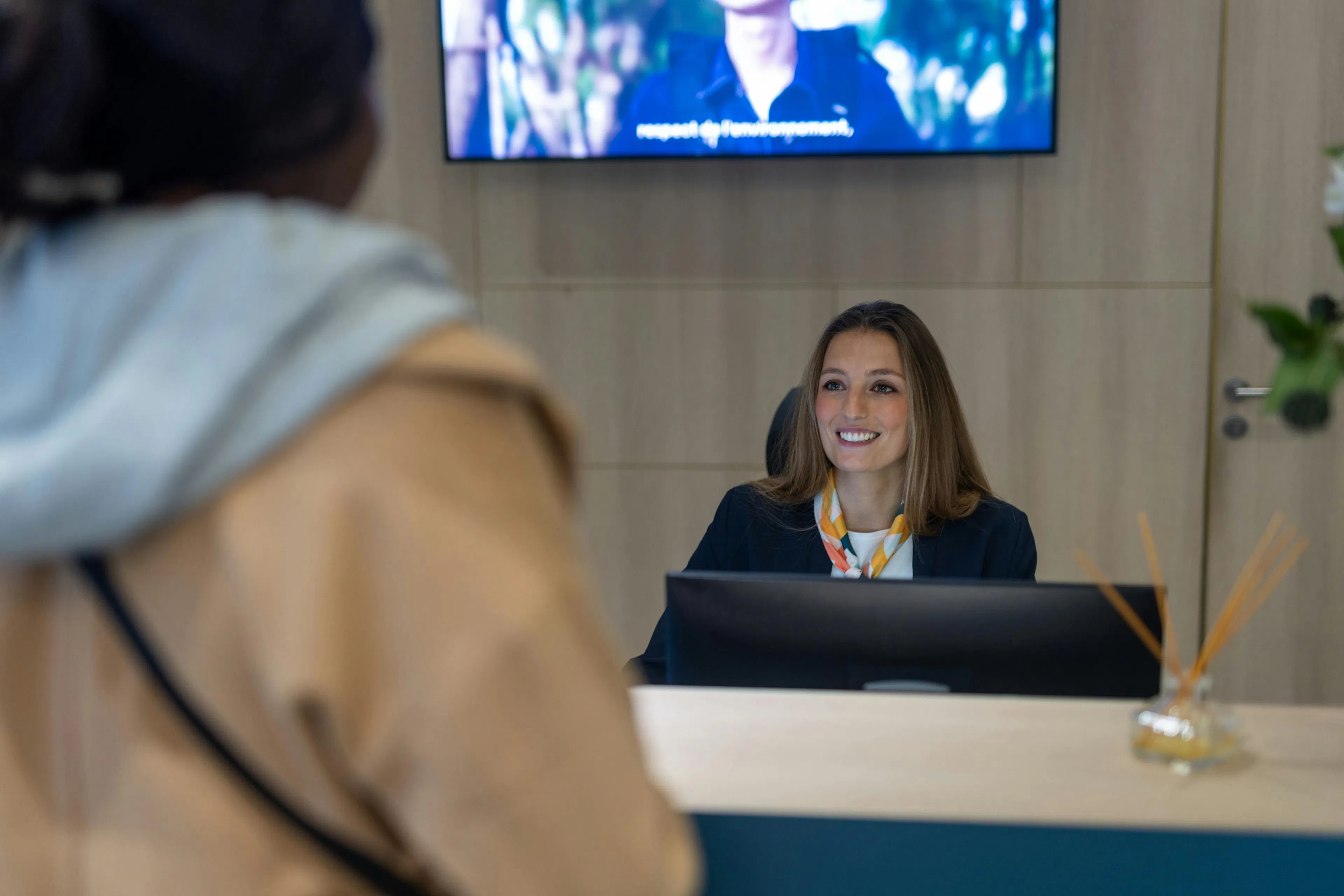 A receptionist at the reception desk of a company welcoming a visitor