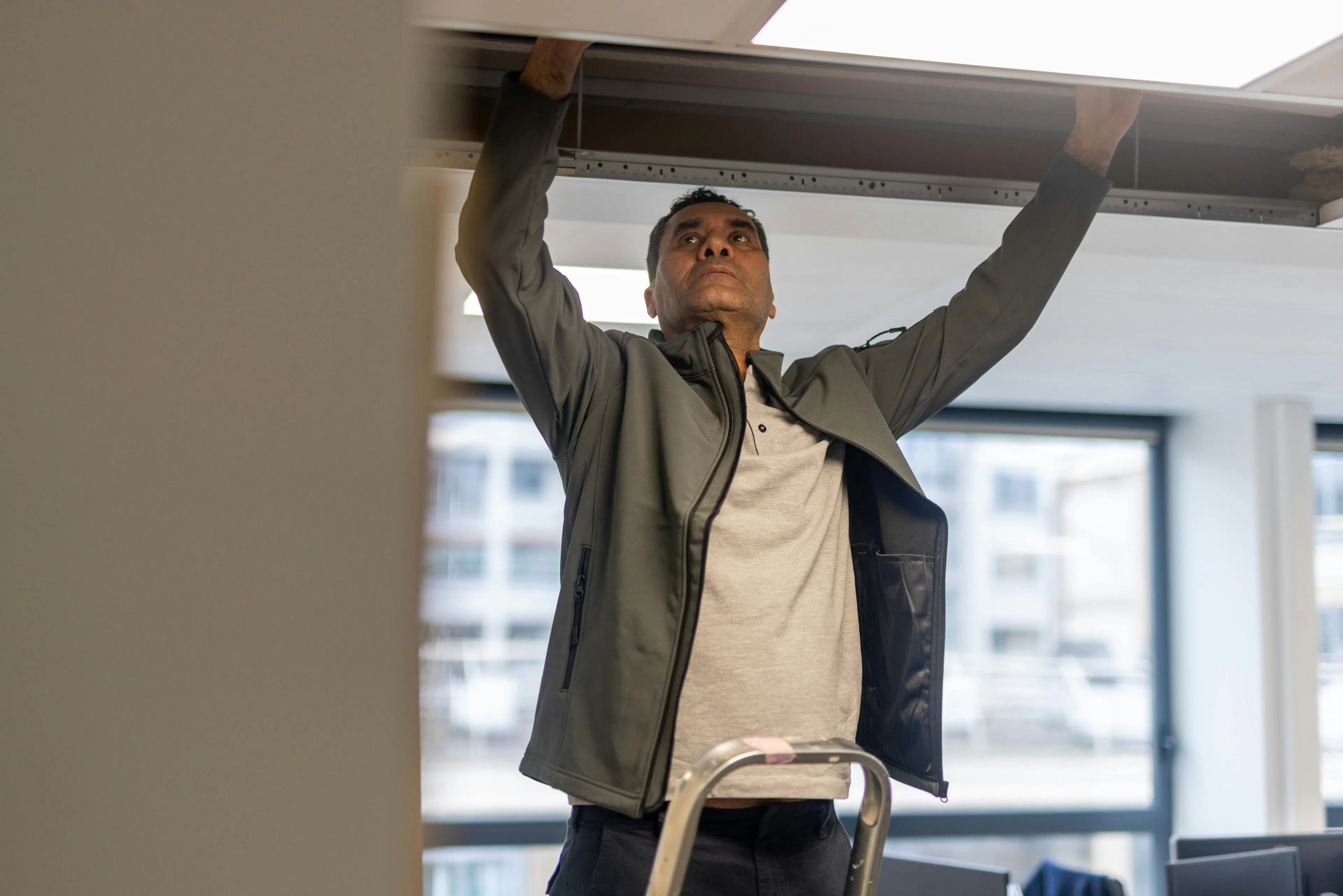 A maintenance agent repairing suspended ceilings in a work environment