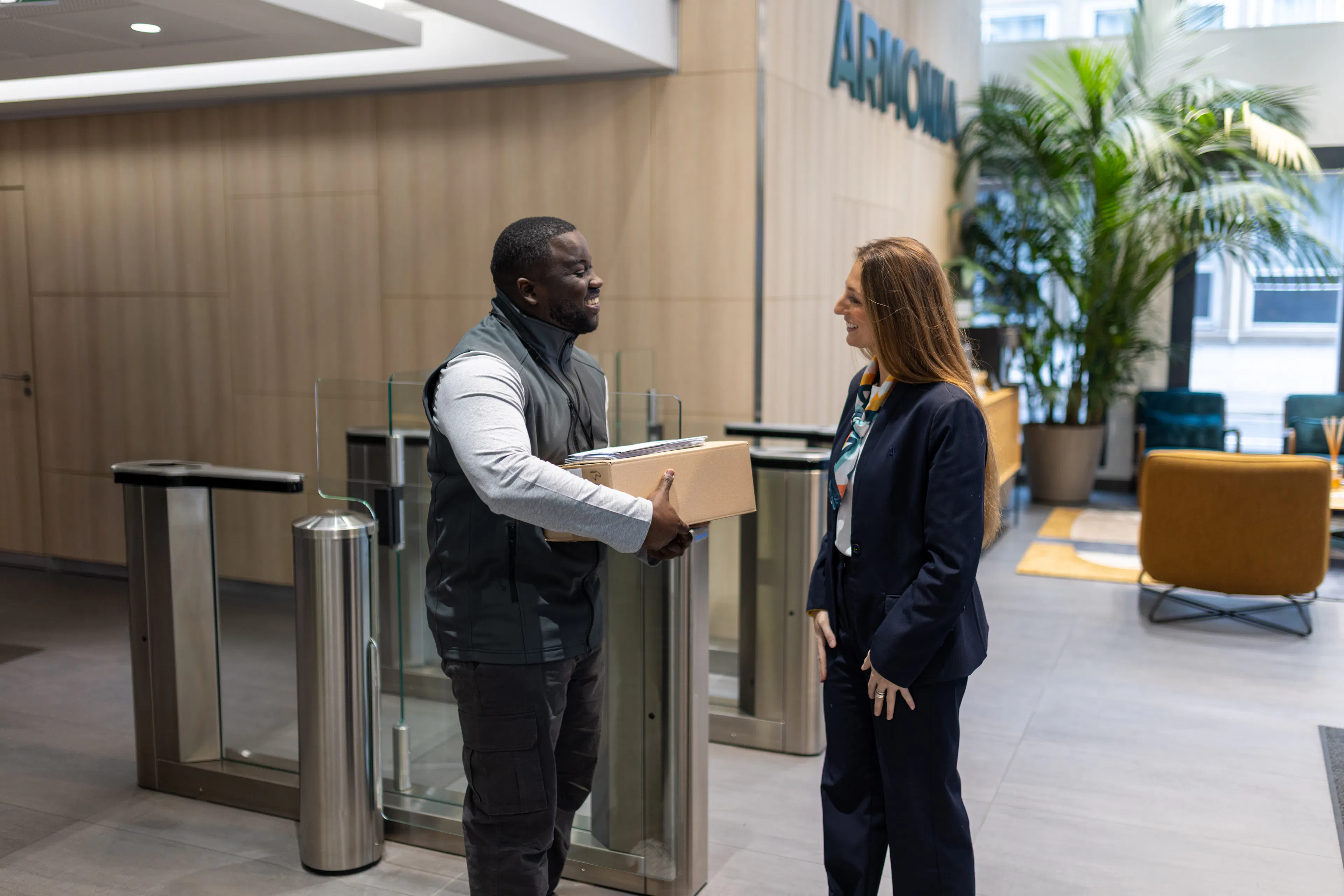 Une hôtesse et un agent de courrier réceptionnant un colis au sein d'un environnement de travail