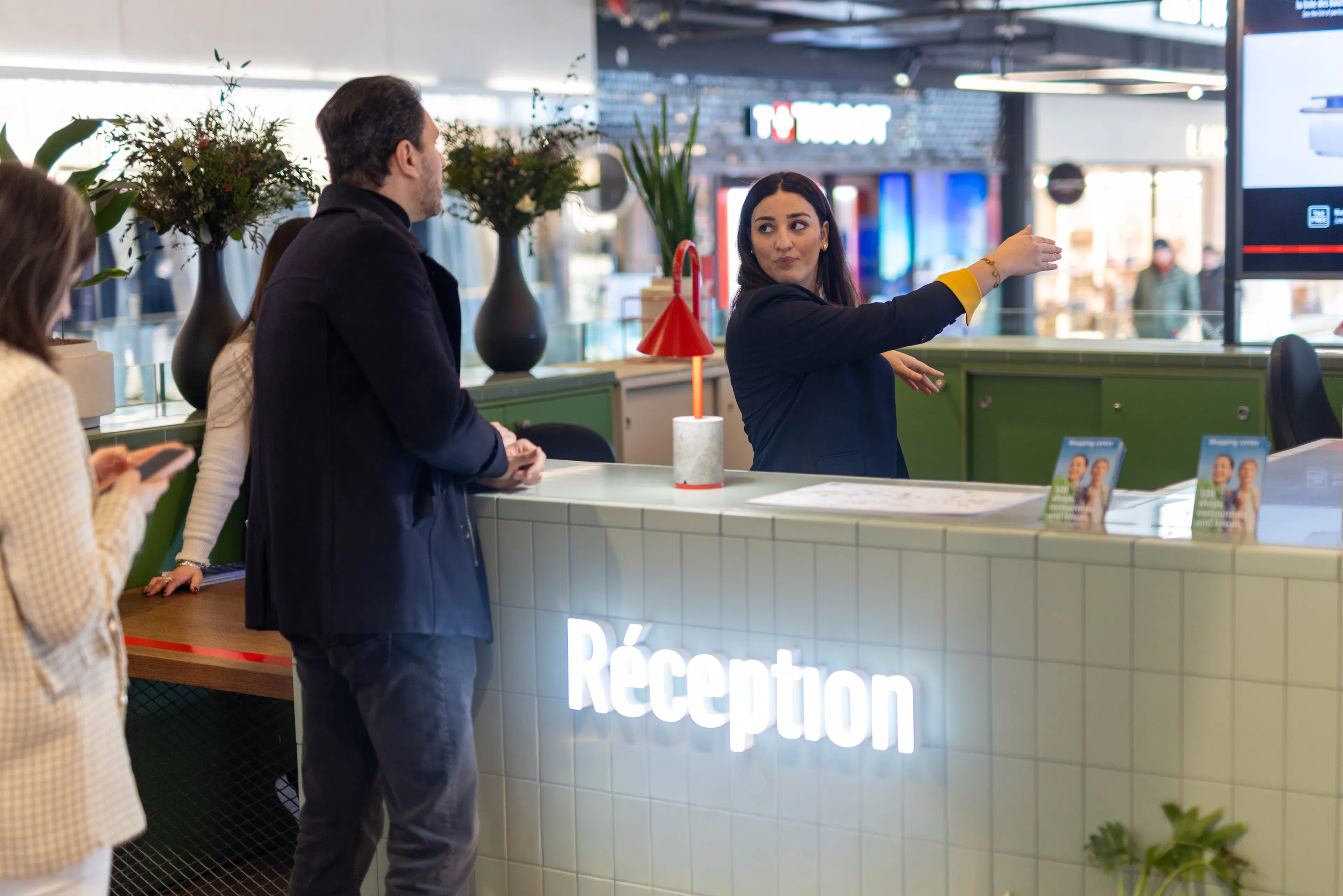 Une hôtesse d'accueil donnant des informations sur l'orientation du centre commercial à un visiteur