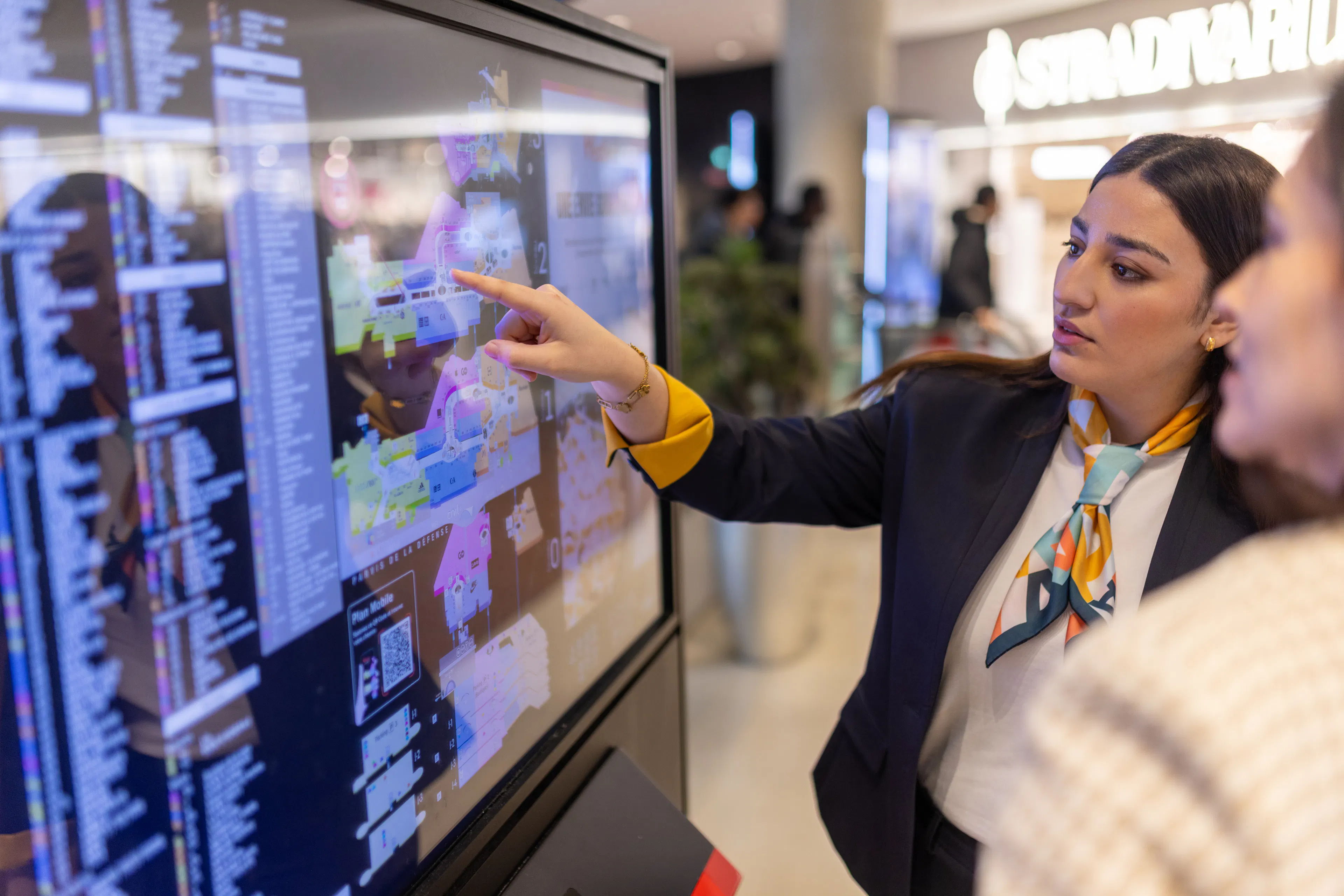 Une hôtesse d'accueil transmettant des informations sur l'orientation du centre commercial à un visiteur