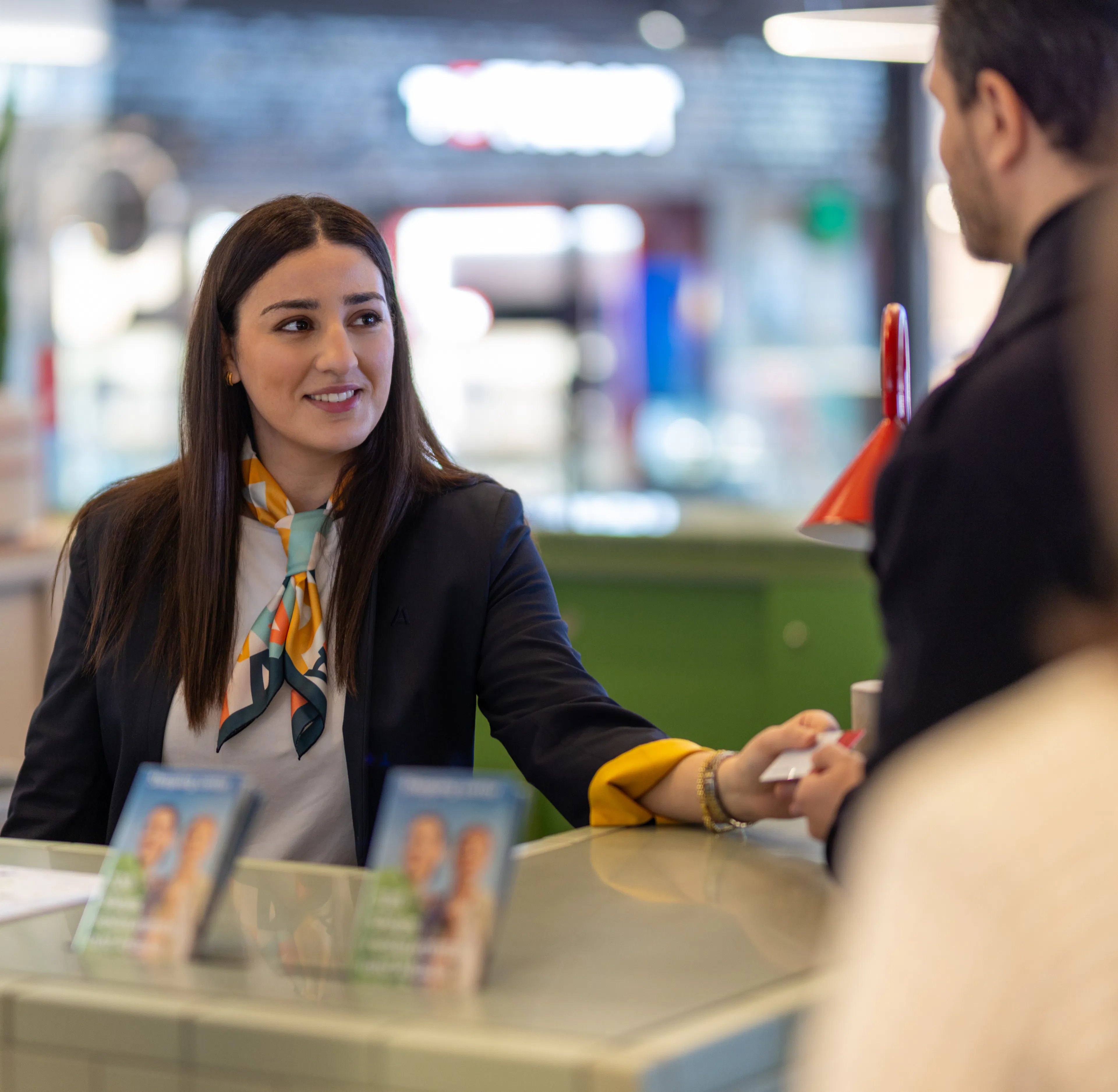Une hôtesse d'accueil remettant une carte cadeau à un visiteur dans un centre commercial