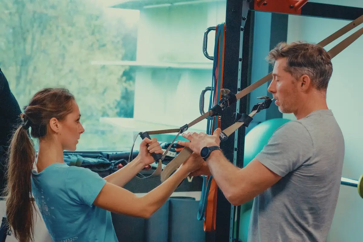 Photographie d’Arnaud guidant un client lors d’un exercice de TRX afin de l’aider à bien positionner ses mains.