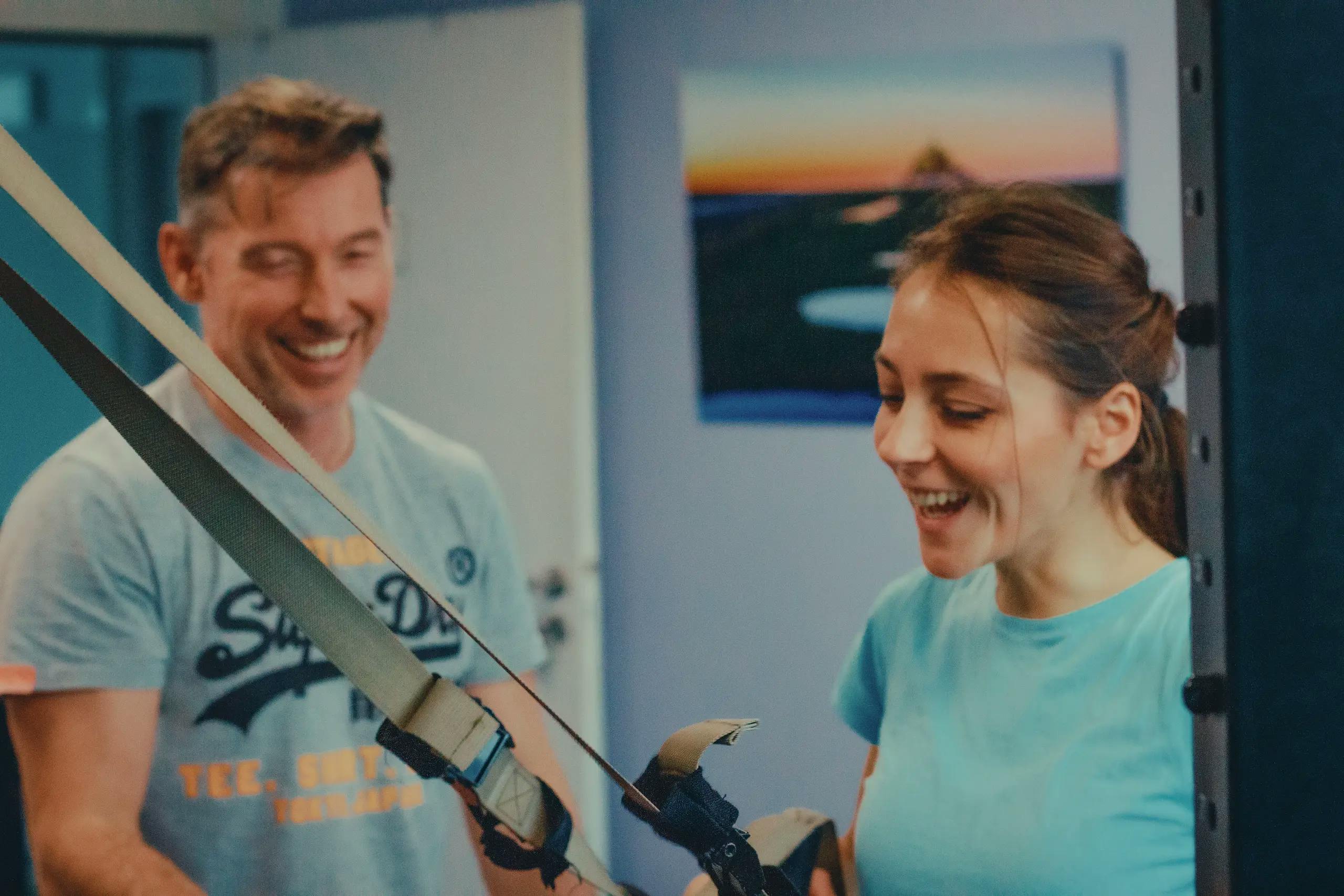 Photographie d’Arnaud guidant un client lors d’un exercice de TRX, dans une ambiance détendue et pleine de rires.